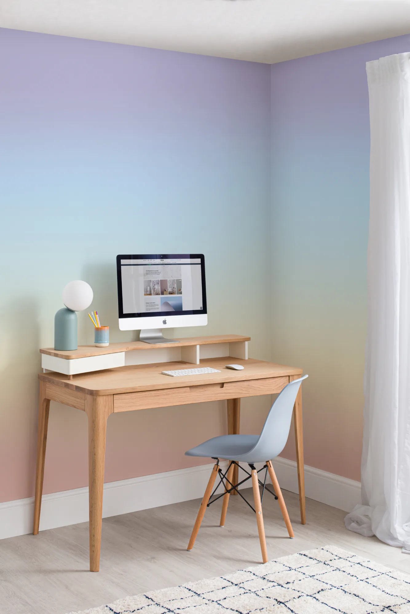 A gradient rainbow ombre mural providing a colorful backdrop to a minimalist desk setup with a chair and computer.