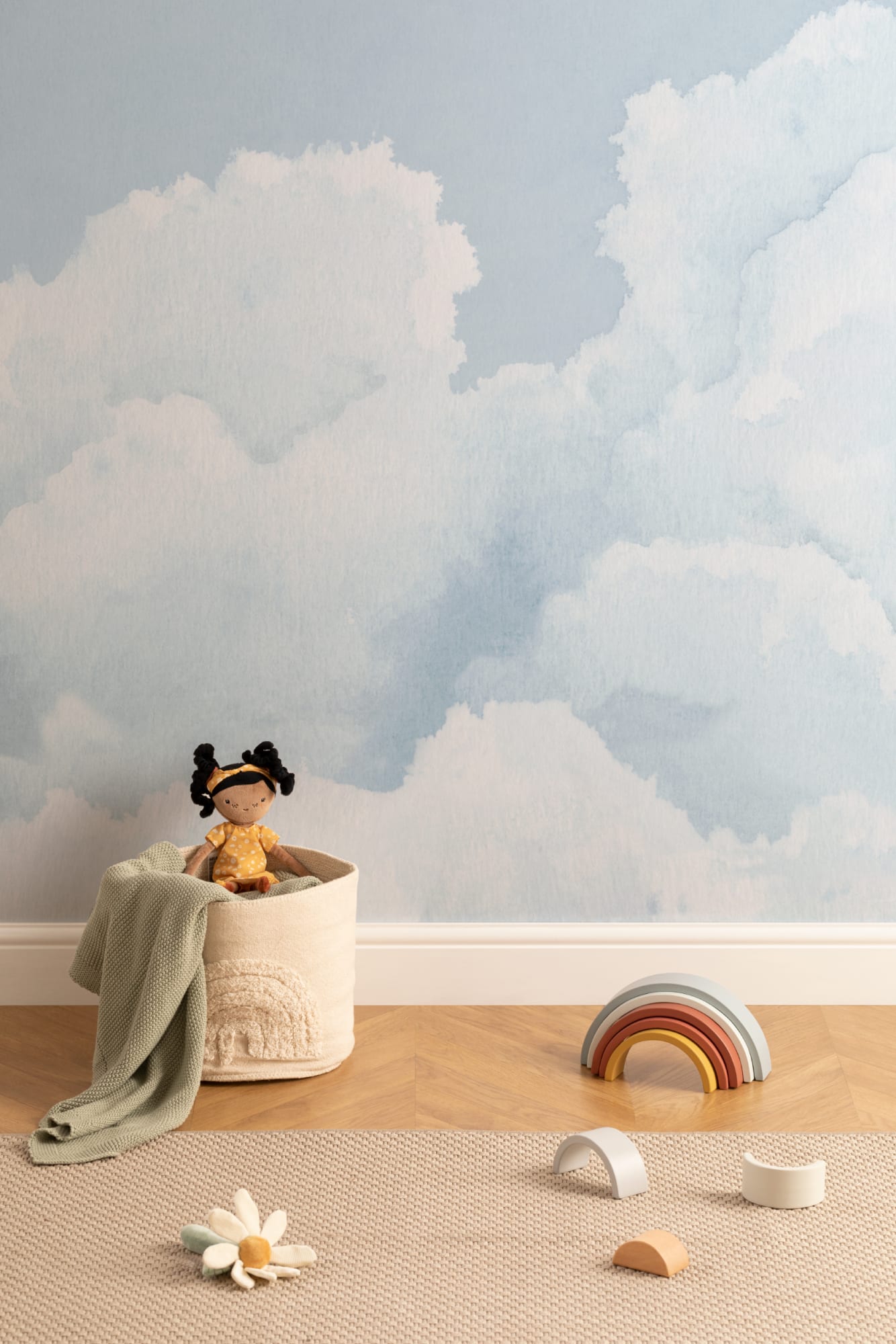 A serene blue cloud mural creates a calming atmosphere in a children's room with soft toys and minimal decor.