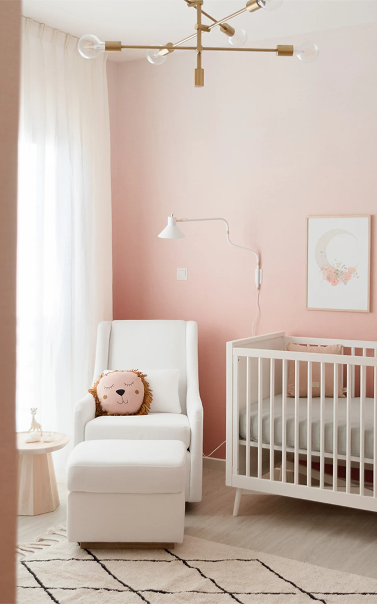 A calming nursery with a pink ombre wall, white furniture, and a cozy armchair.