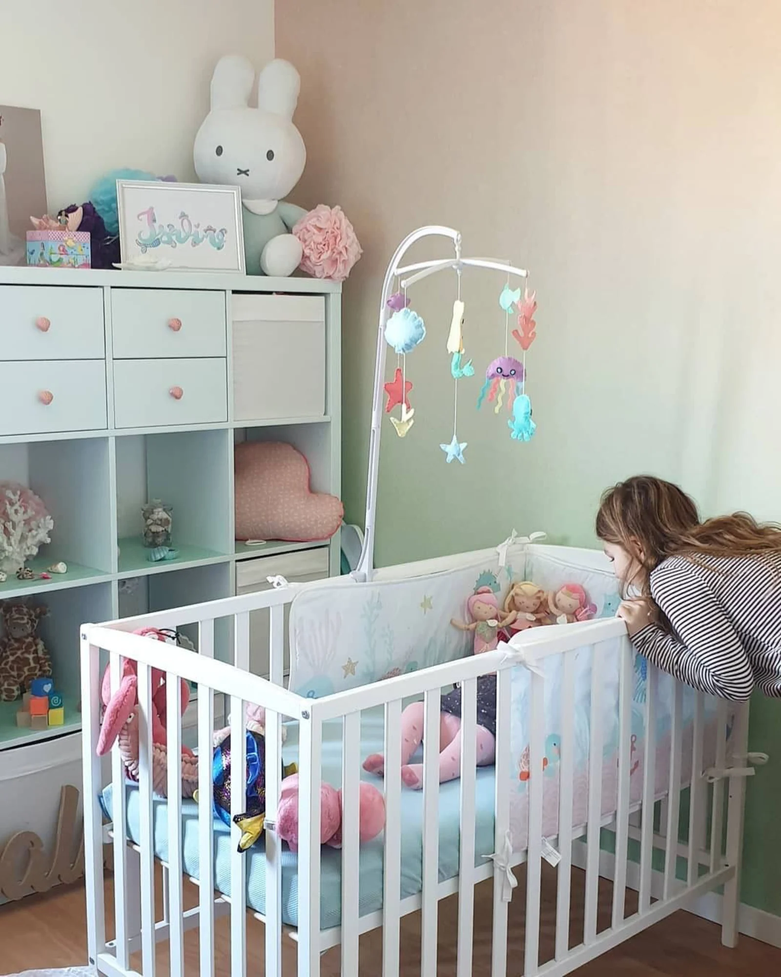 A nursery with a gradient pink and green ombre wall, featuring soft, minimalistic decor.