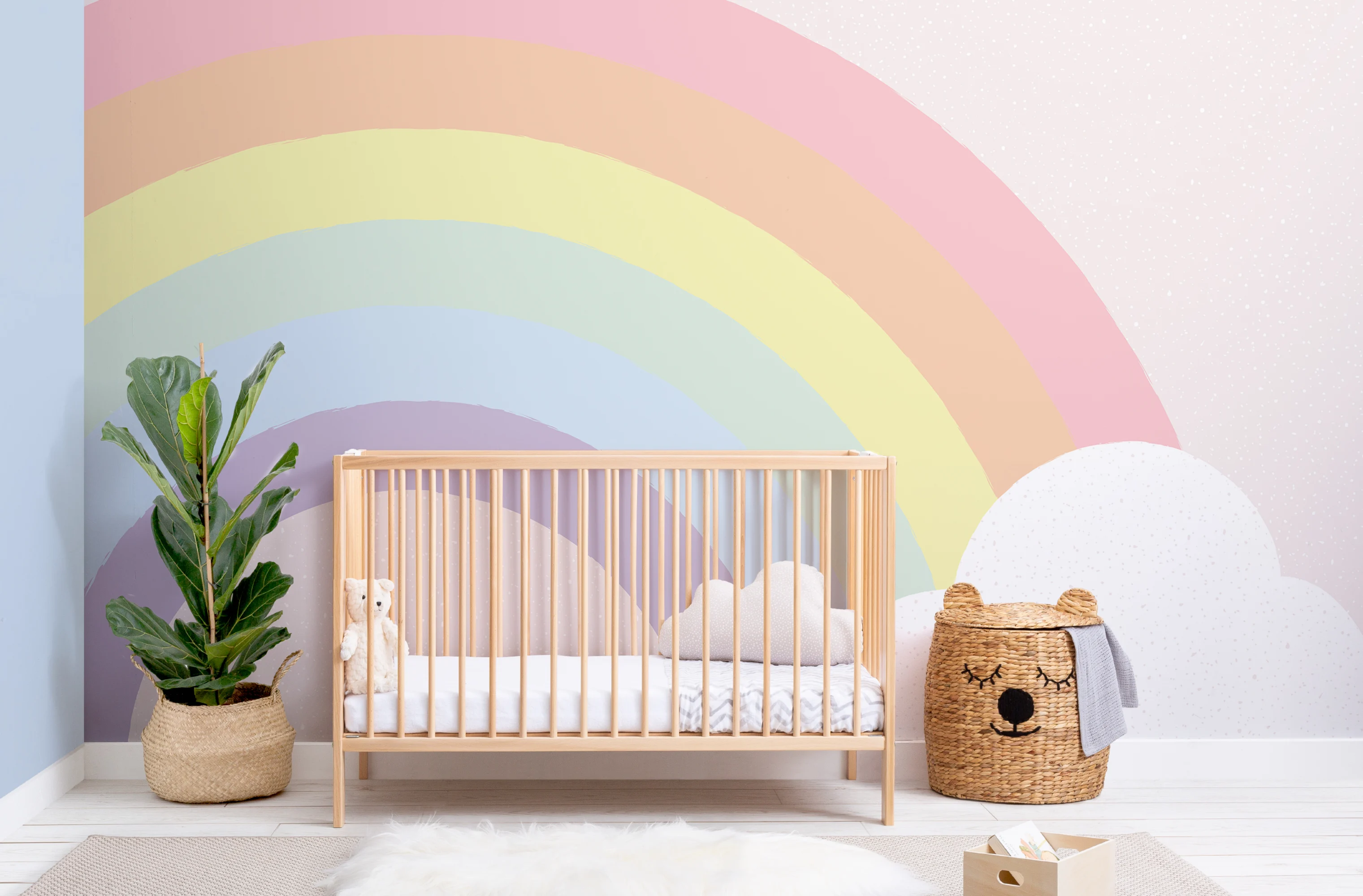 A cheerful nursery with a pastel rainbow mural, wooden crib, and woven bear basket.