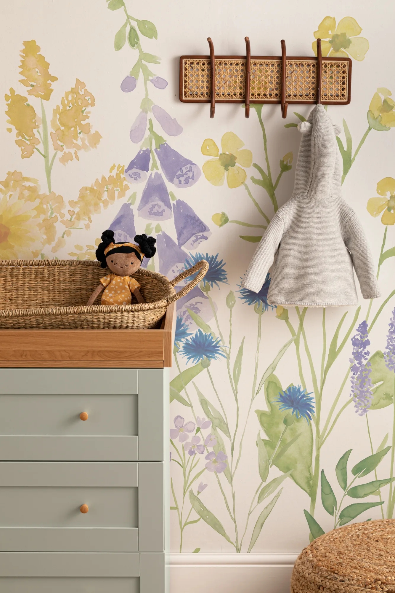 A charming nursery with a wildflower mural, wicker decor, and a pastel green changing station.