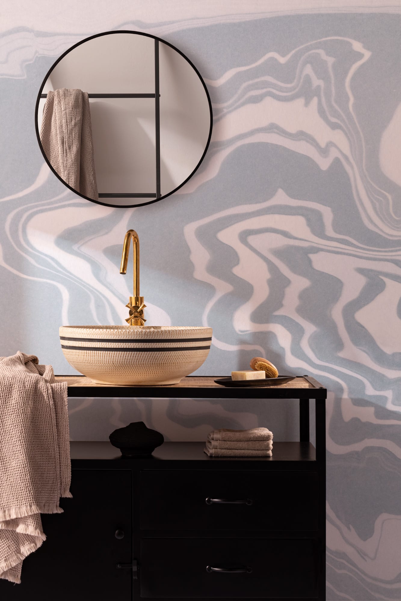 A Japandi-style bathroom with a blue abstract wallpaper, round mirror, and textured bowl sink.