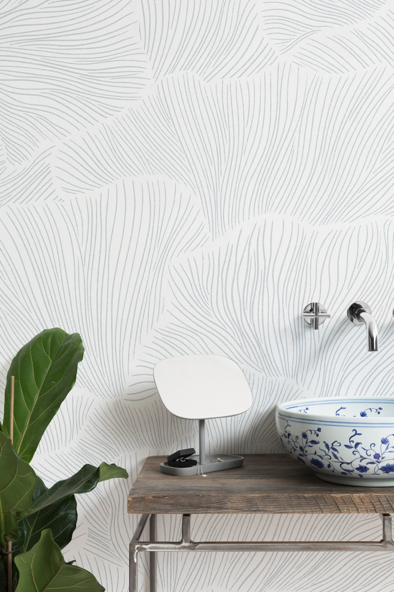 A minimalist Japandi style bathroom with white wallpaper featuring fine blue lines, a rustic vanity, and a blue floral sink.