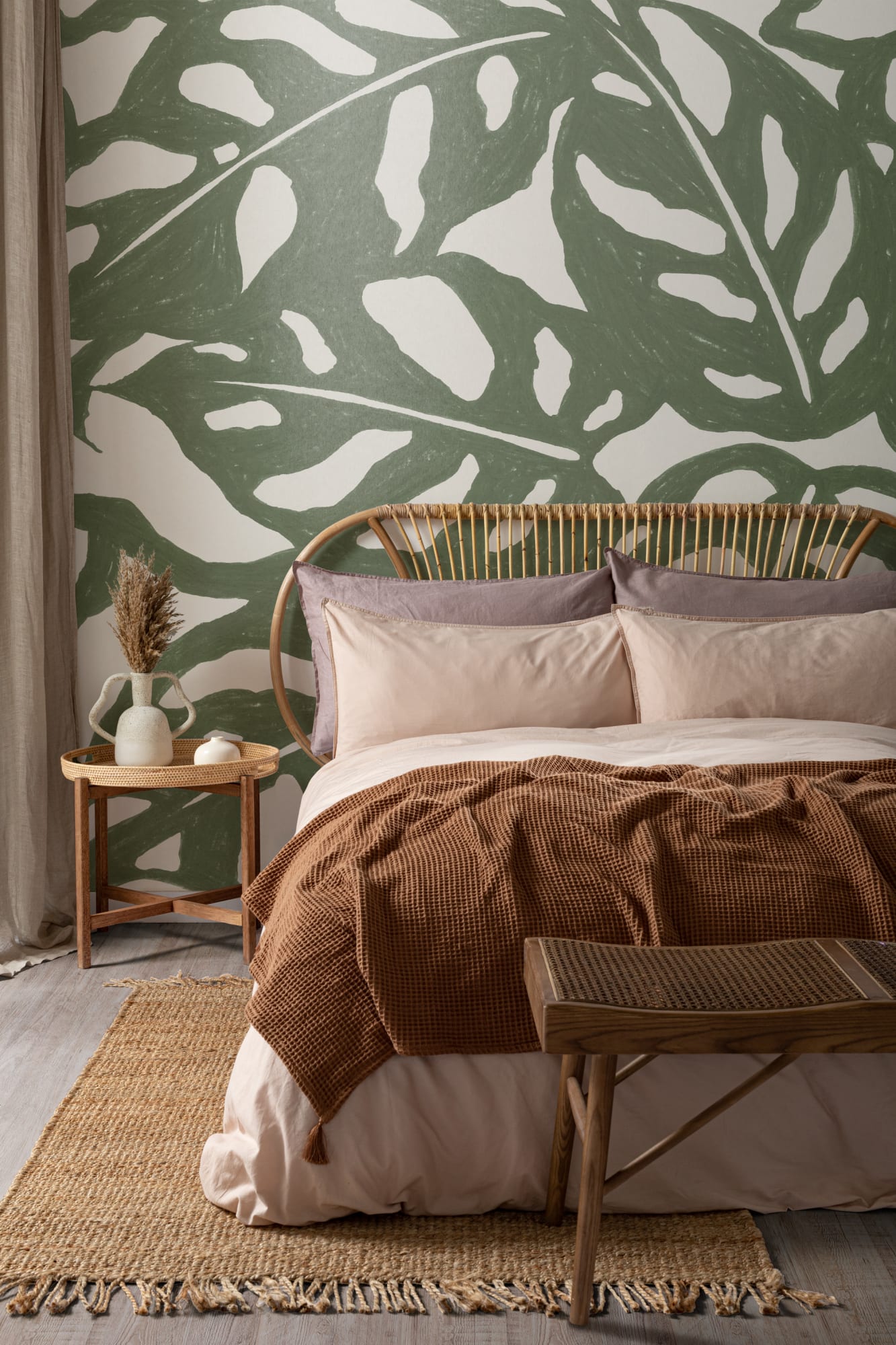 A cozy bedroom with a bold monstera leaf wall mural in green, complemented by neutral bedding and warm wooden accents.