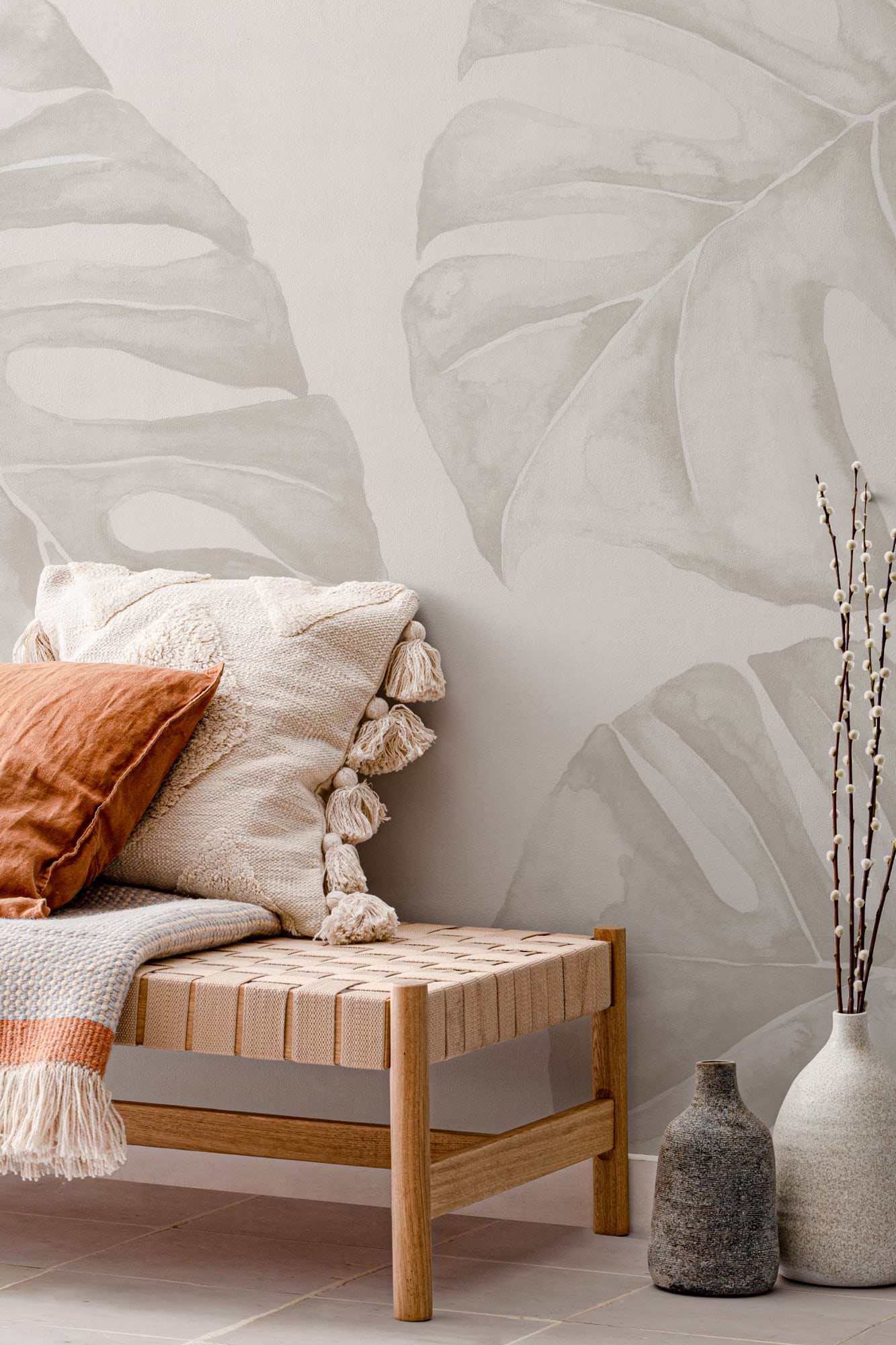 A minimalist biophilic hallway featuring a soft neutral-toned wall mural of oversized tropical leaves paired with natural woven decor and ceramic accents.