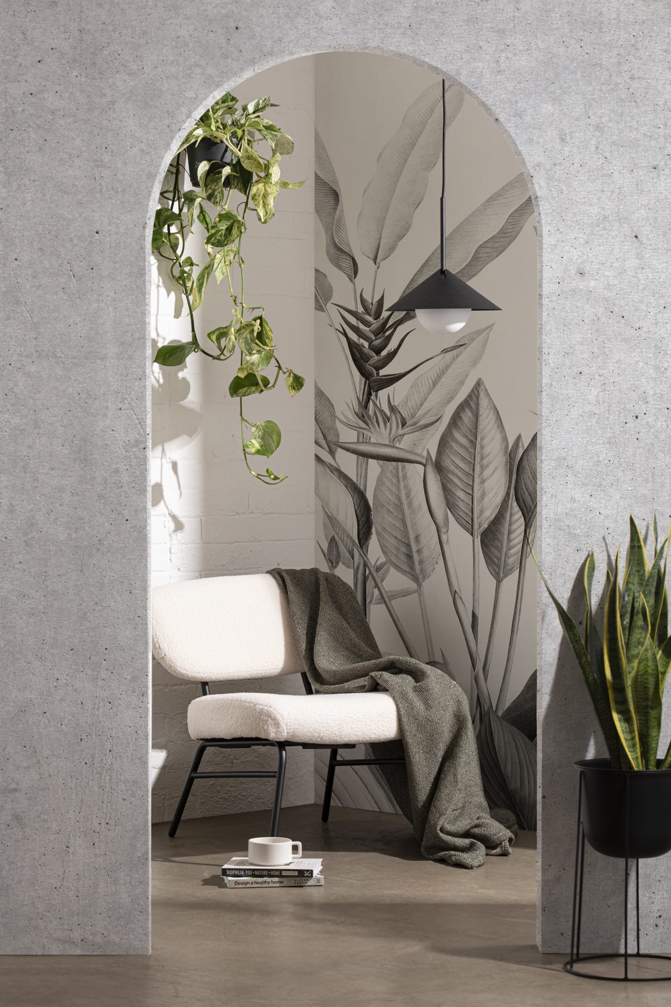 A serene space with a monochromatic biophilic wall mural behind a soft chair framed by a concrete archway, accented with lush hanging plants.
