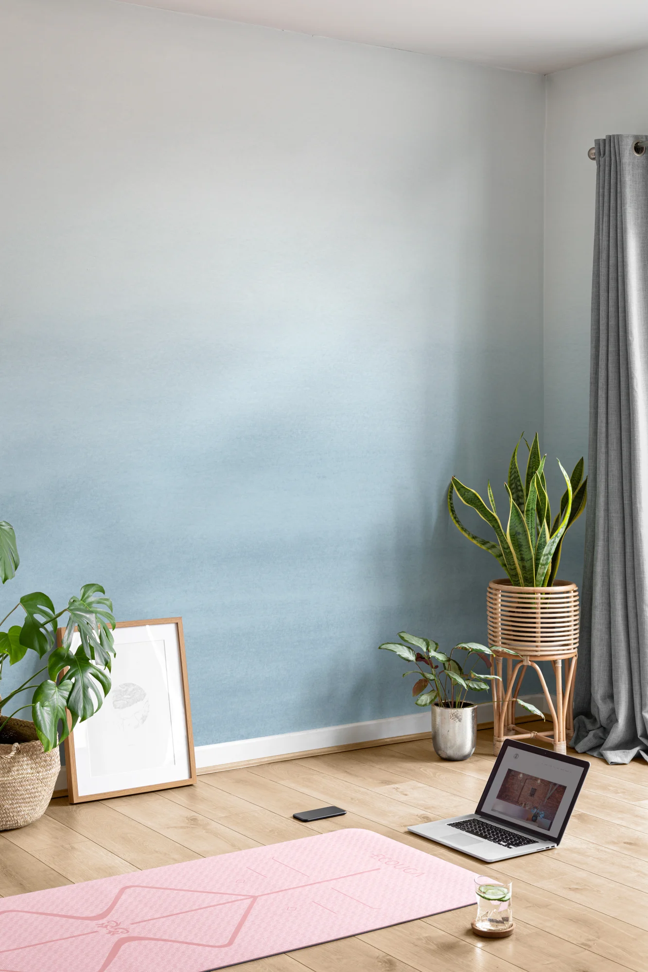 A minimalist yoga space with a calming blue watercolor mural, wooden flooring, and lush potted plants.