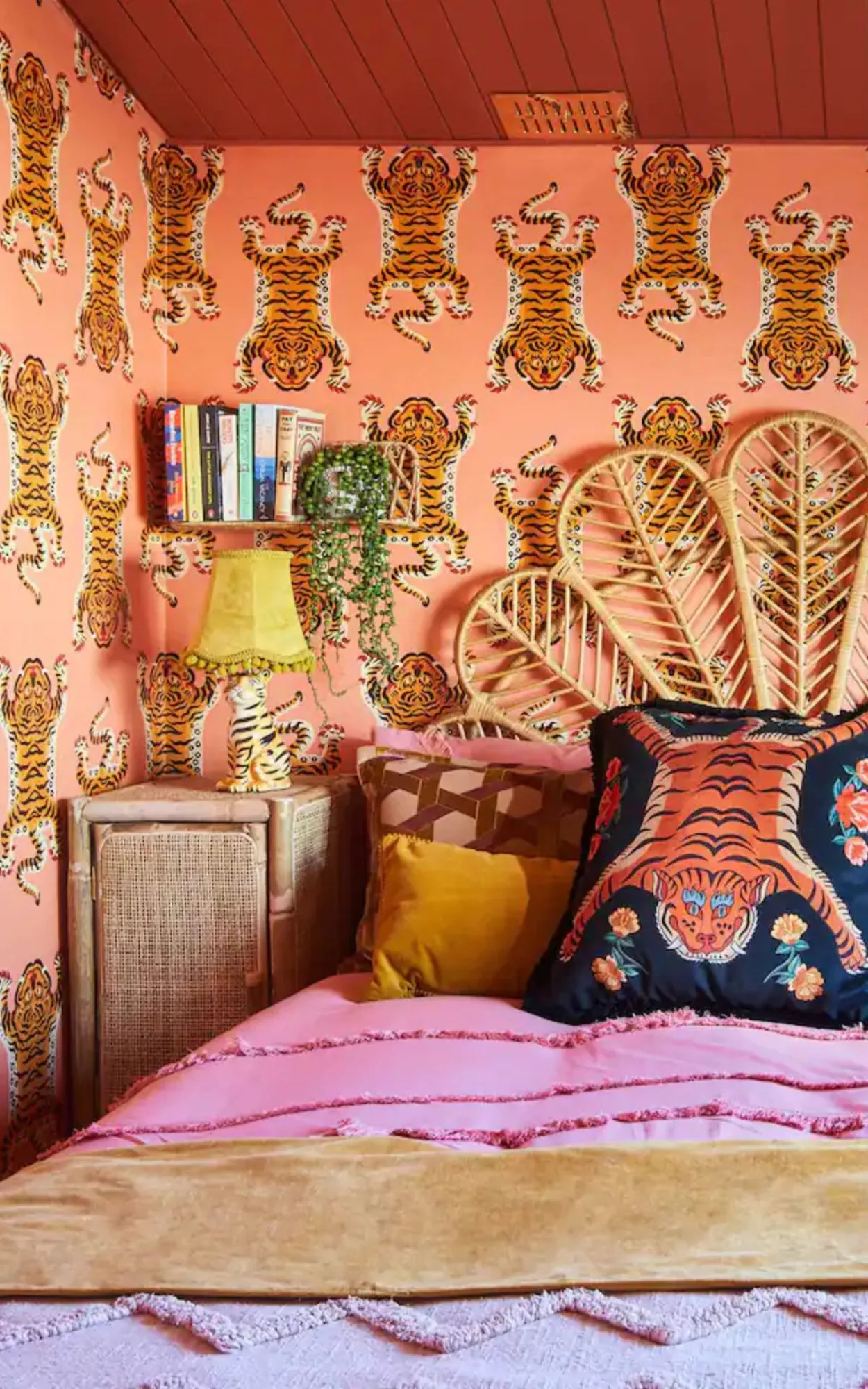 A maximalist bedroom featuring playful orange tiger wallpaper, a rattan headboard, and bold, colorful textiles.