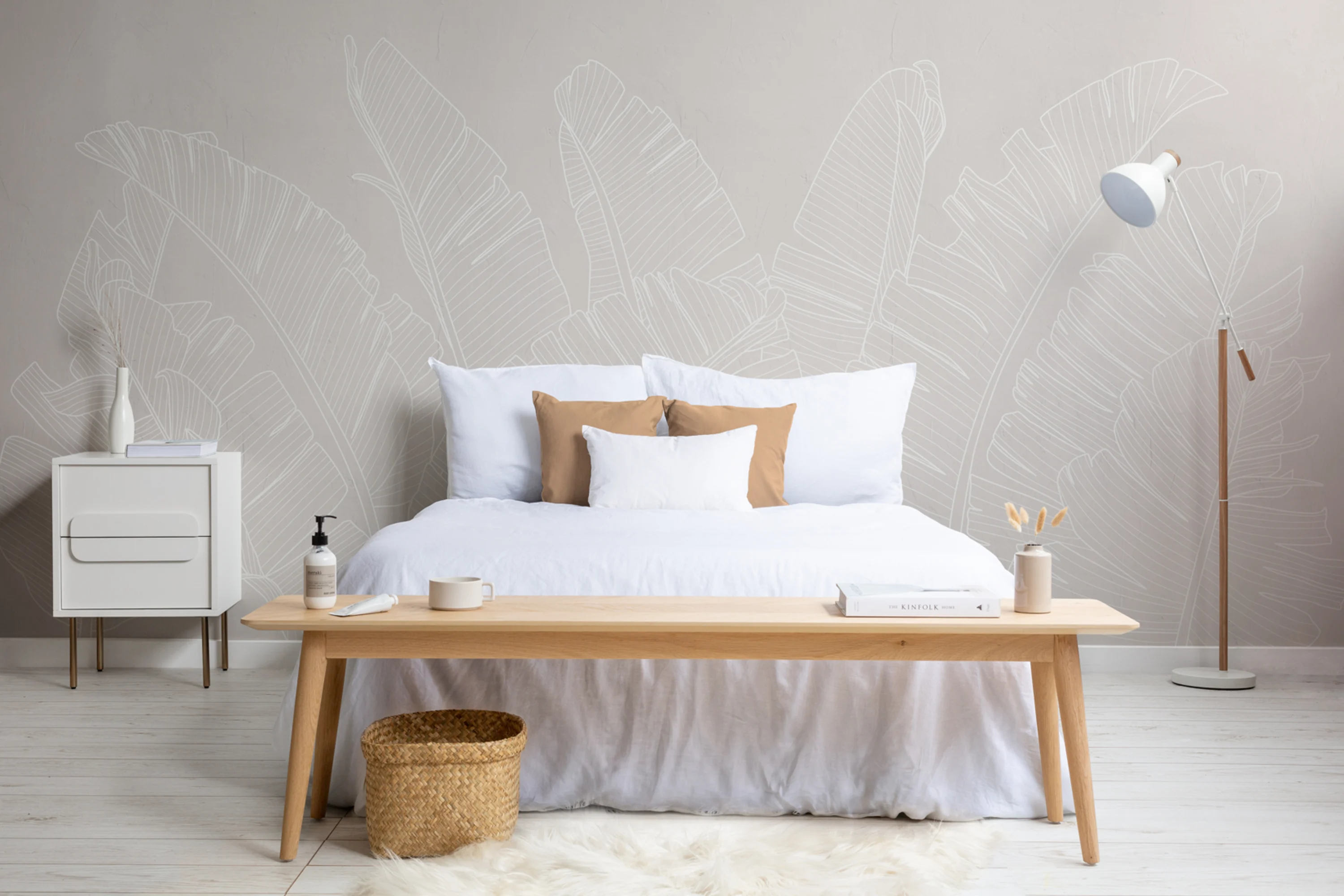 A minimalist bedroom with a neutral-toned wall mural featuring subtle banana leaf outlines, accented by simple wooden furniture and cozy textiles.