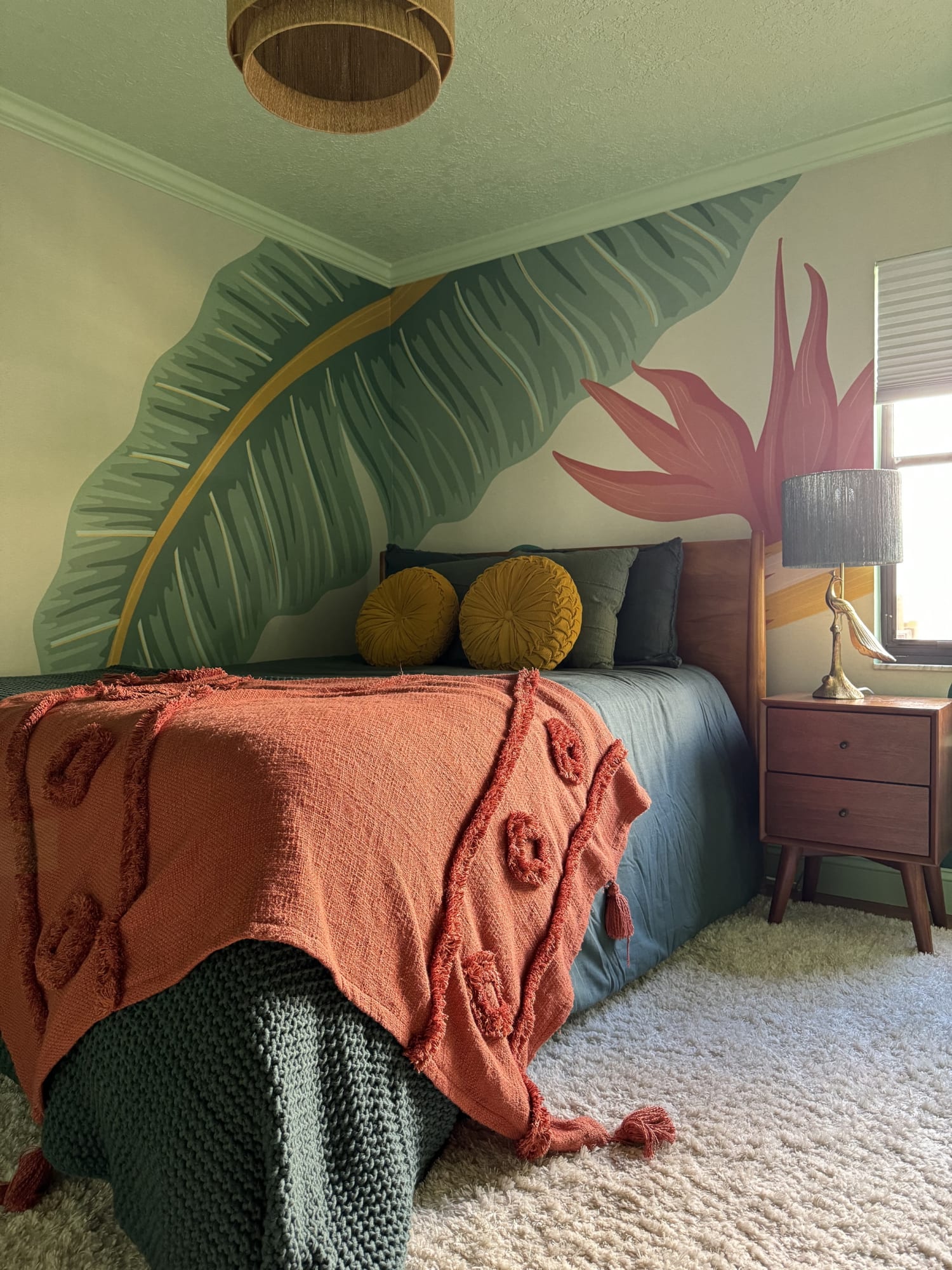 A bedroom featuring a tropical leaf and flower mural paired with bold bedding and mid-century decor.