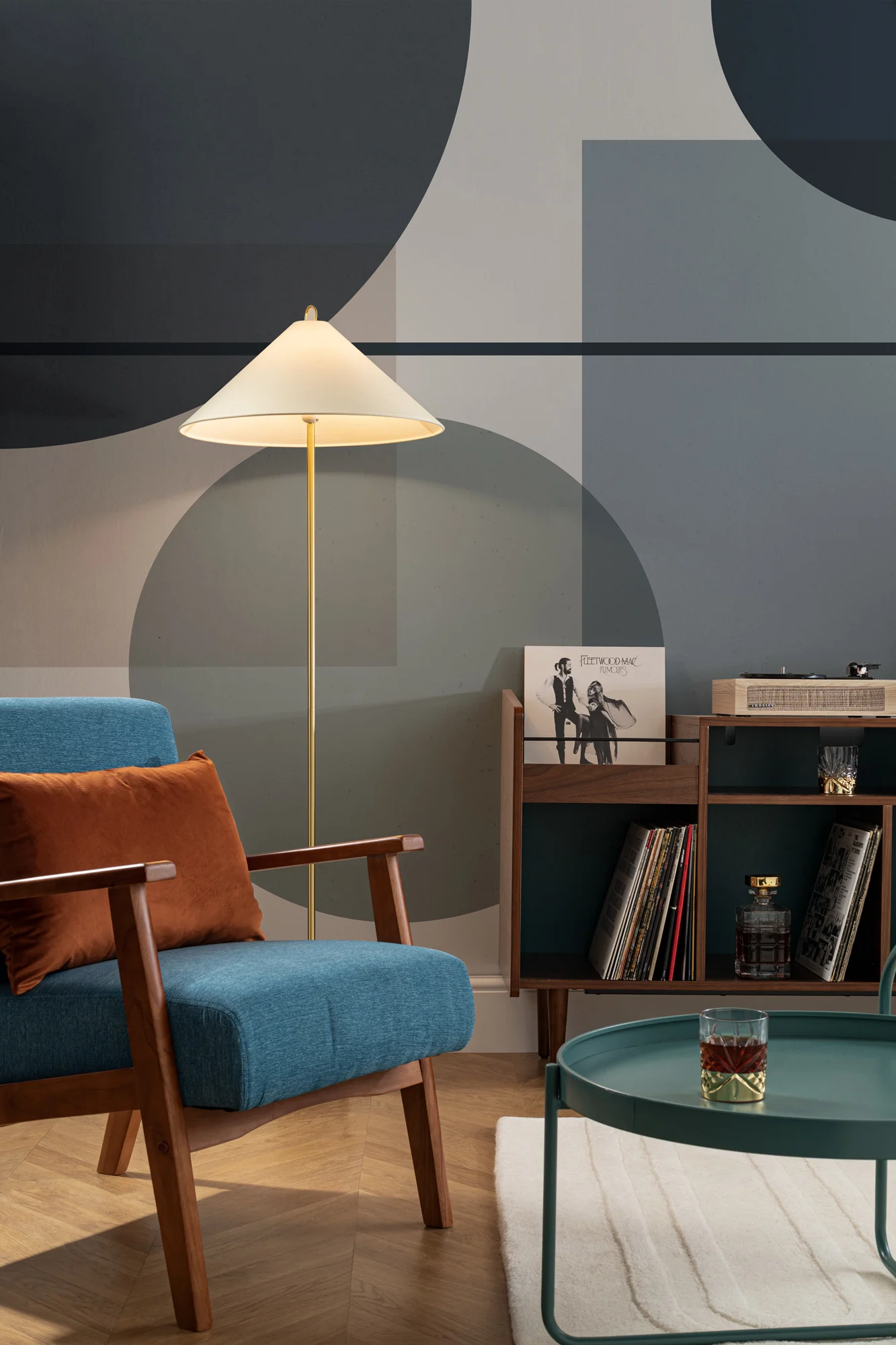 A stylish living space with a bold geometric mural in shades of blue and gray, featuring a mid-century armchair, floor lamp, and a vintage record player.