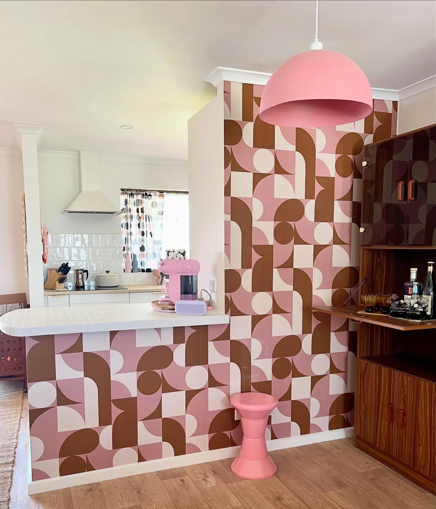 A Mid-Century modern style inspired kitchen with pink and brown geometric wallpaper, a matching pink pendant light, and vintage-style decor.