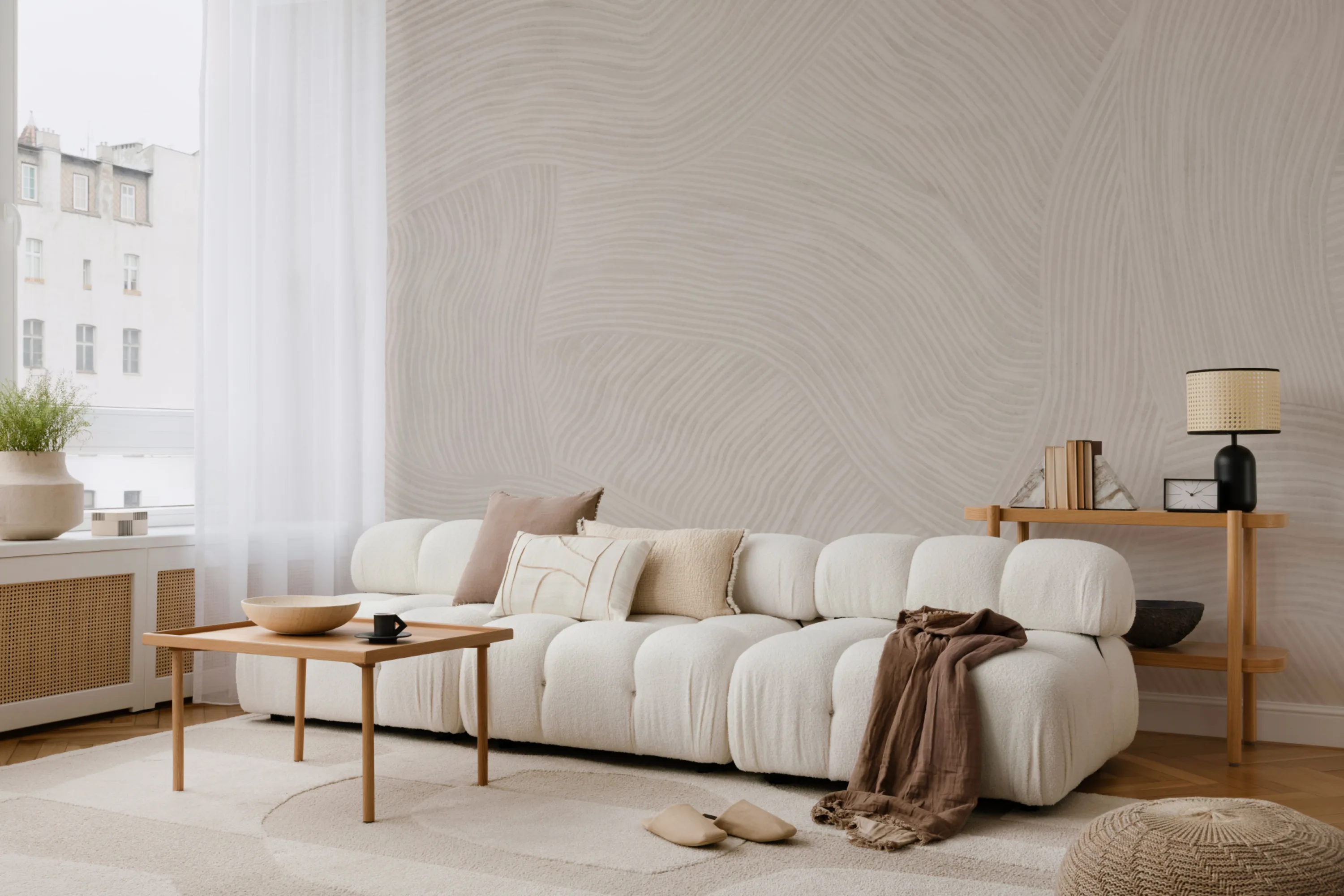 An airy living room with a subtle beige Japandi style mural, a cozy tufted sofa, and natural wood accents.
