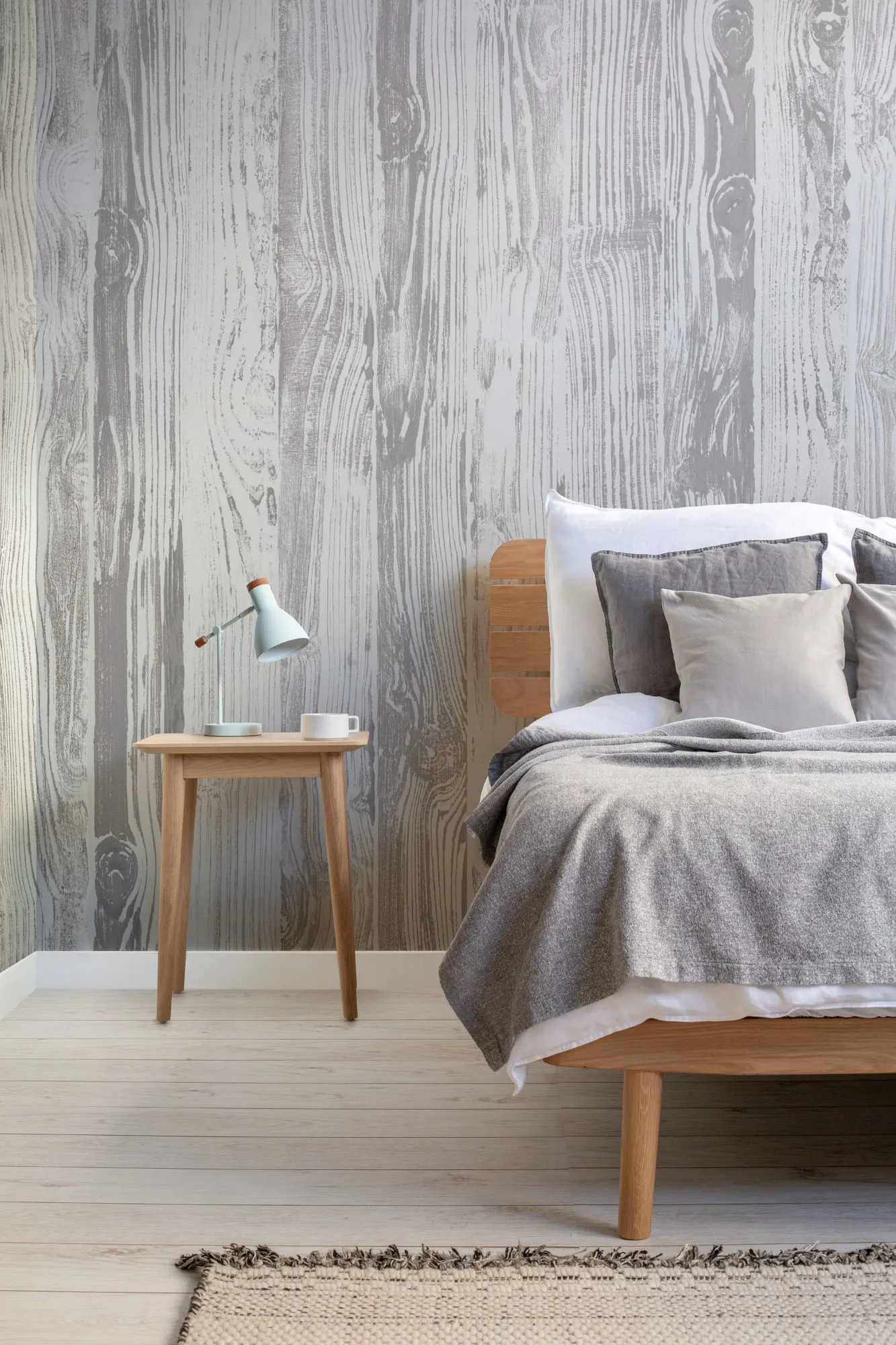 A minimalist Scandi style bedroom featuring a gray wood grain wallpaper, a wooden bed frame, and simple white and gray linens.