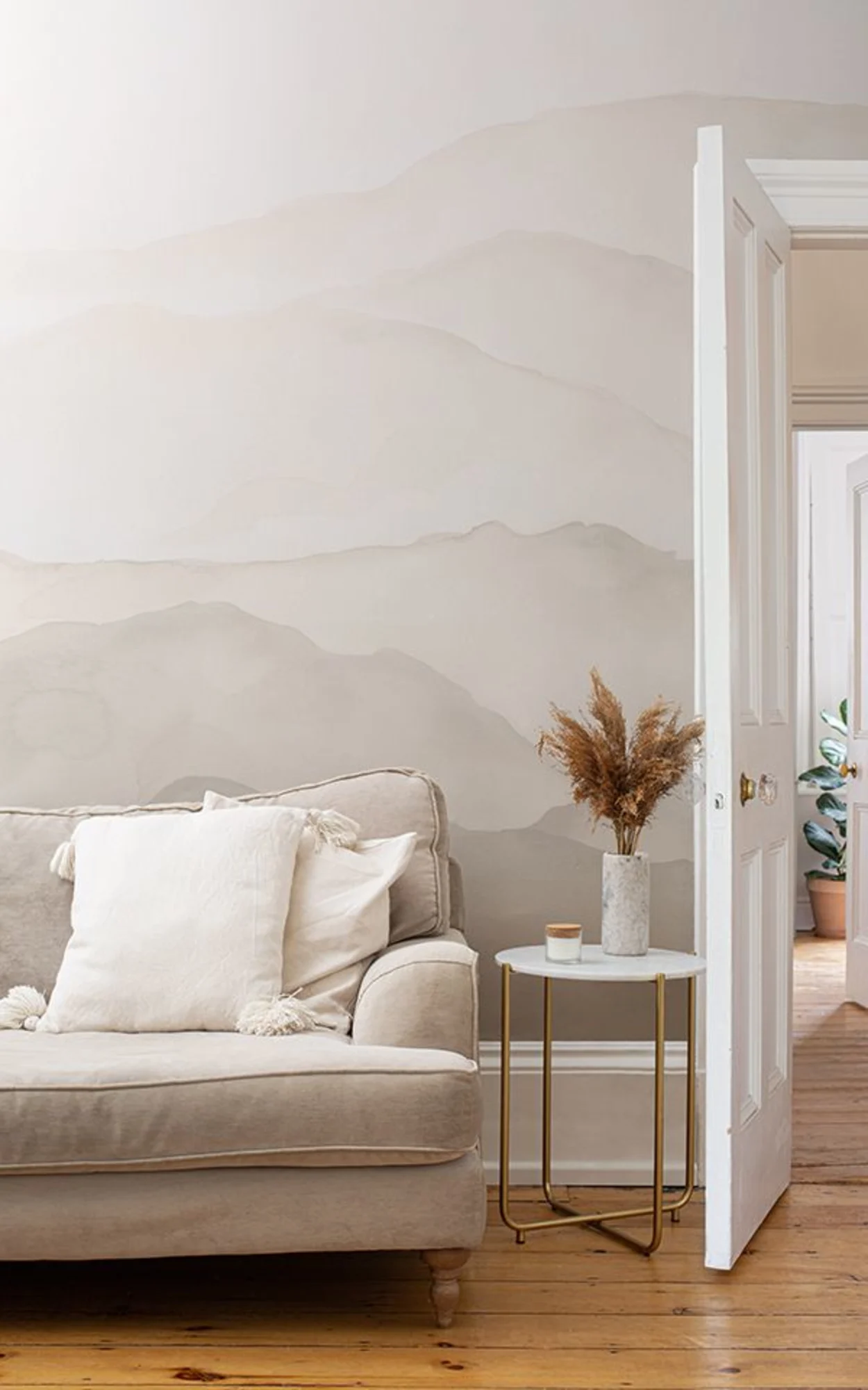 A neutral-toned Scandi style living room with a beige abstract wall mural, a cozy sofa, and a side table styled with dried florals.