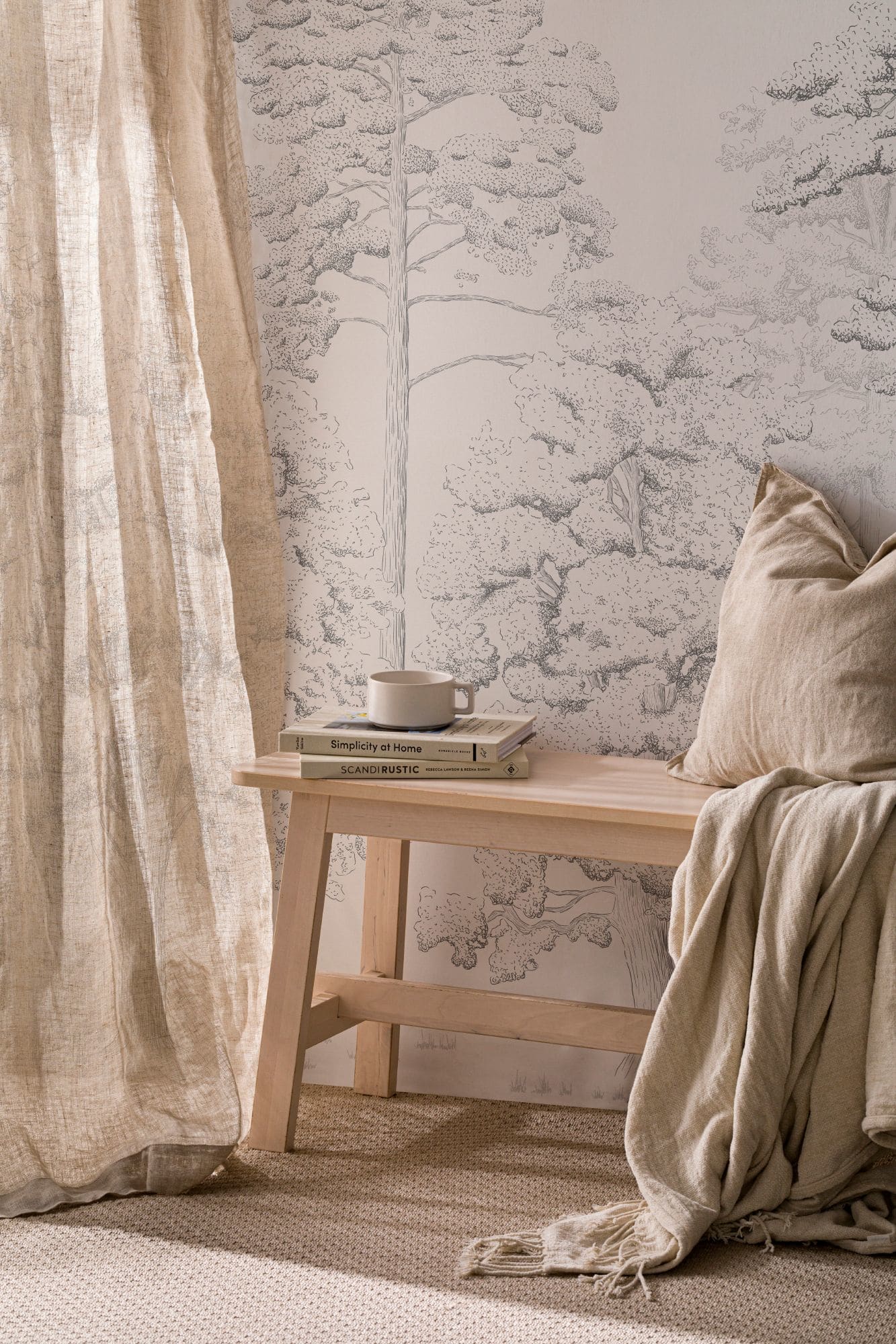 A serene corner in a Scandi style room with a hand-drawn forest mural, a bench styled with neutral cushions, and natural light.
