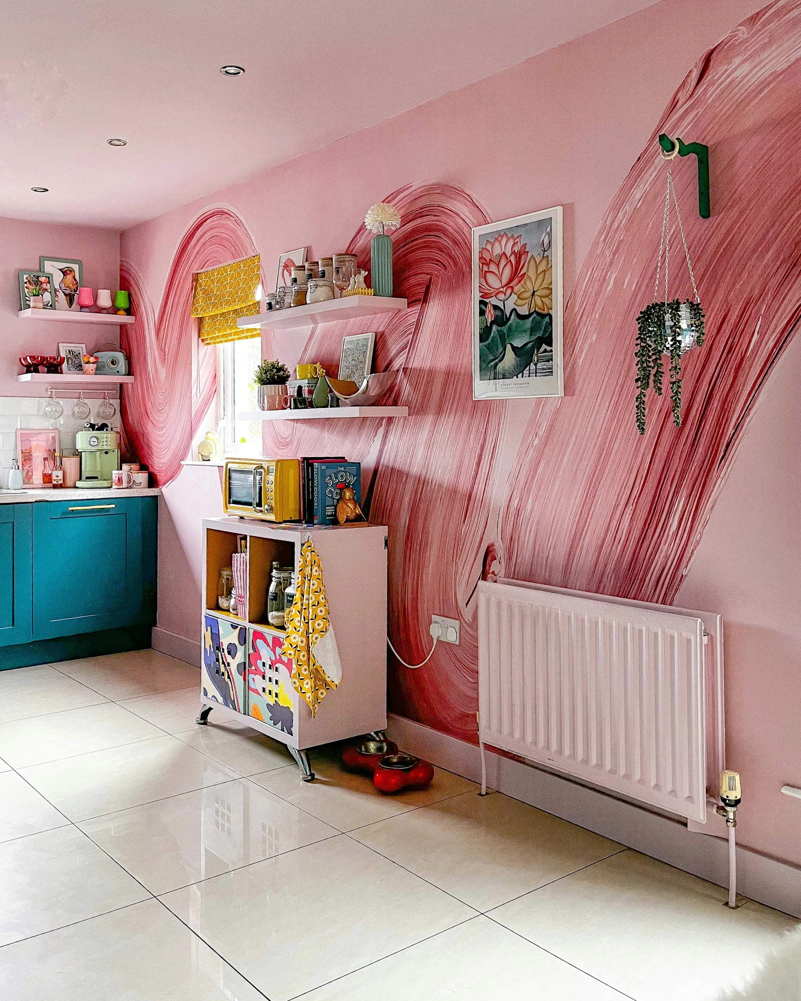 A maximalist kitchen with a bold pink wall mural featuring sweeping brushstrokes, complemented by colorful decor and open shelving.
