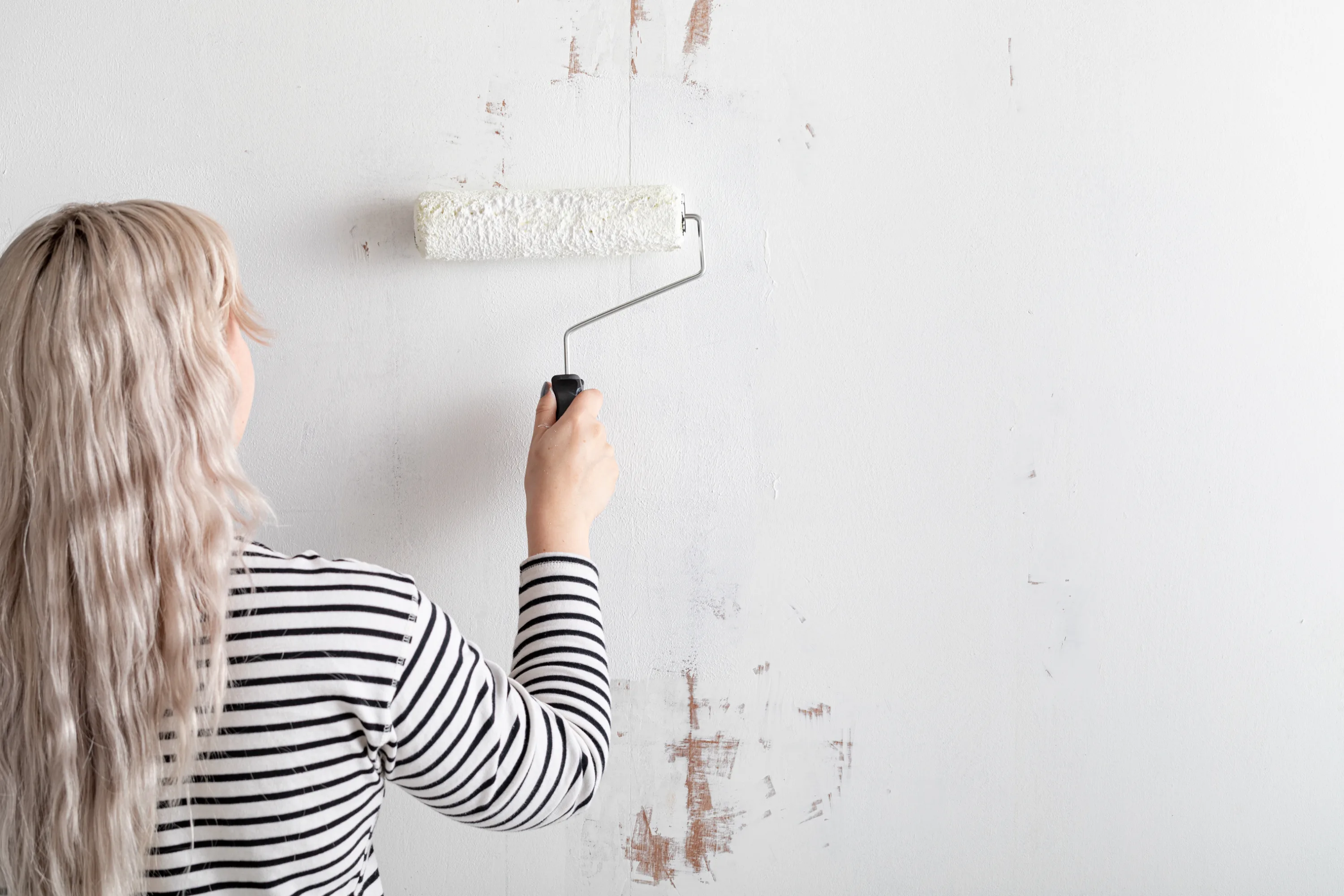 Woman priming a textured wall with a roller while wearing a striped shirt.
