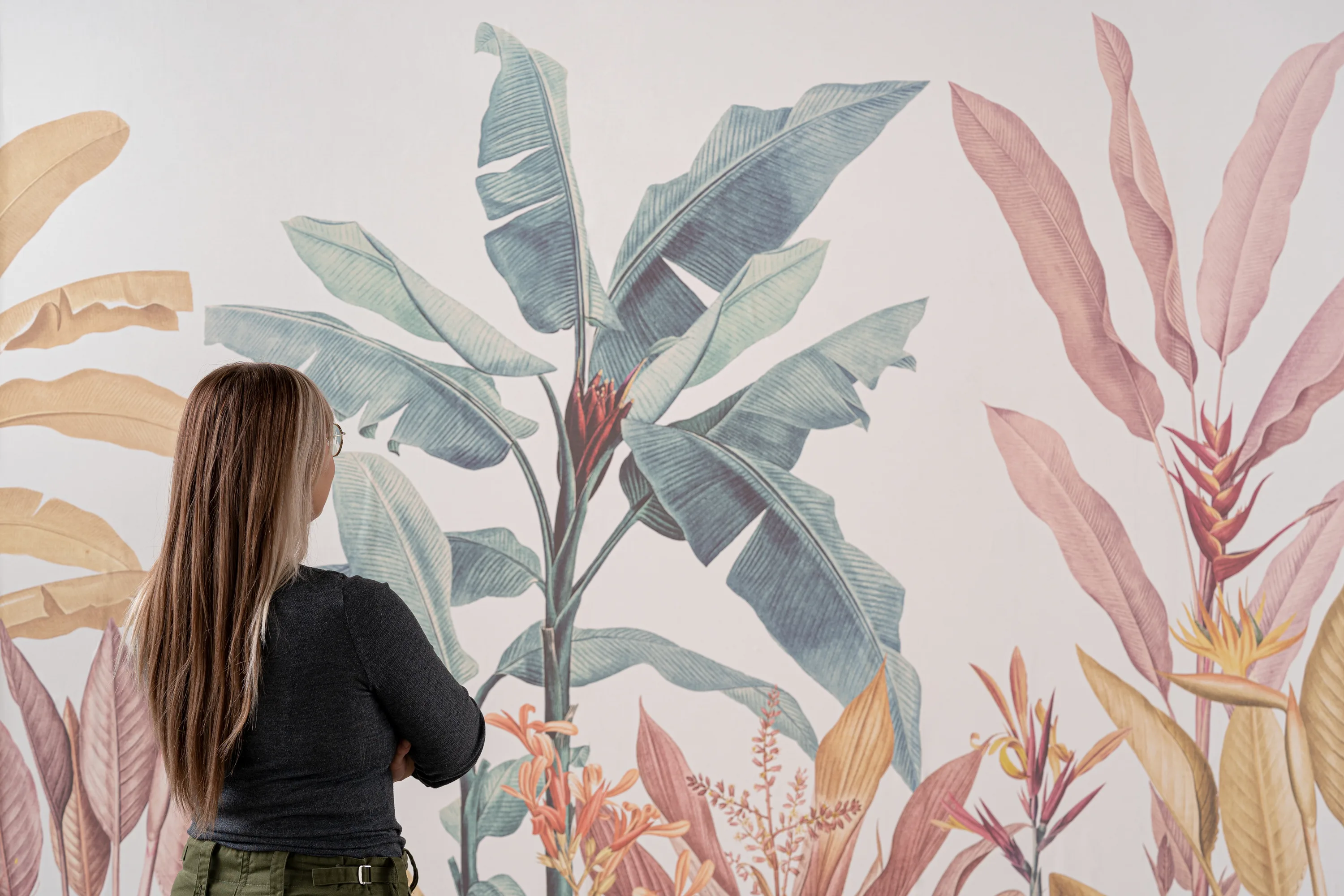 Woman admiring a tropical wallpaper with large banana leaves and colorful botanical elements.