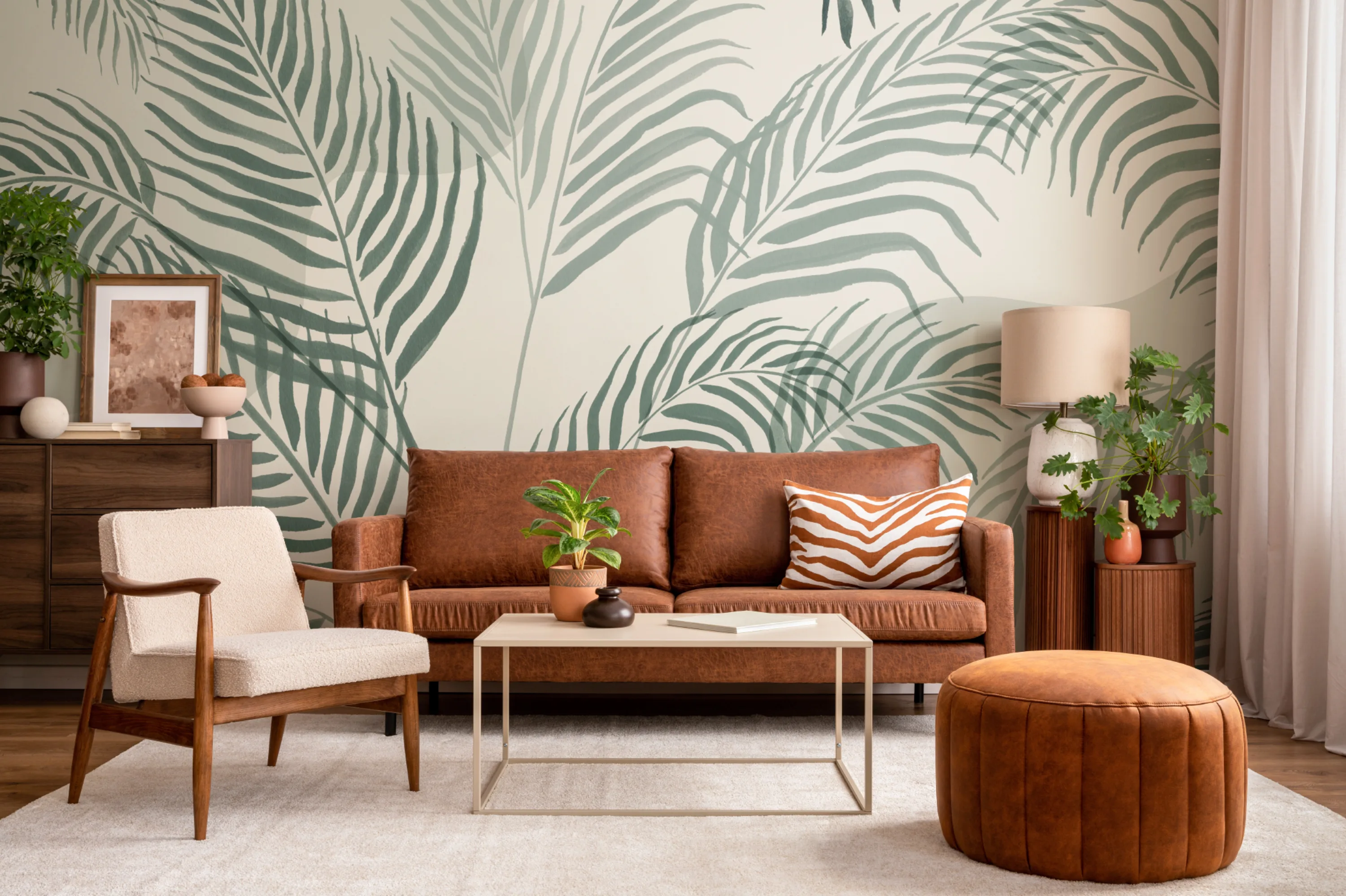 A modern living room with a bold palm leaf mural in green tones, featuring a leather sofa, textured armchair, and warm wooden accents.