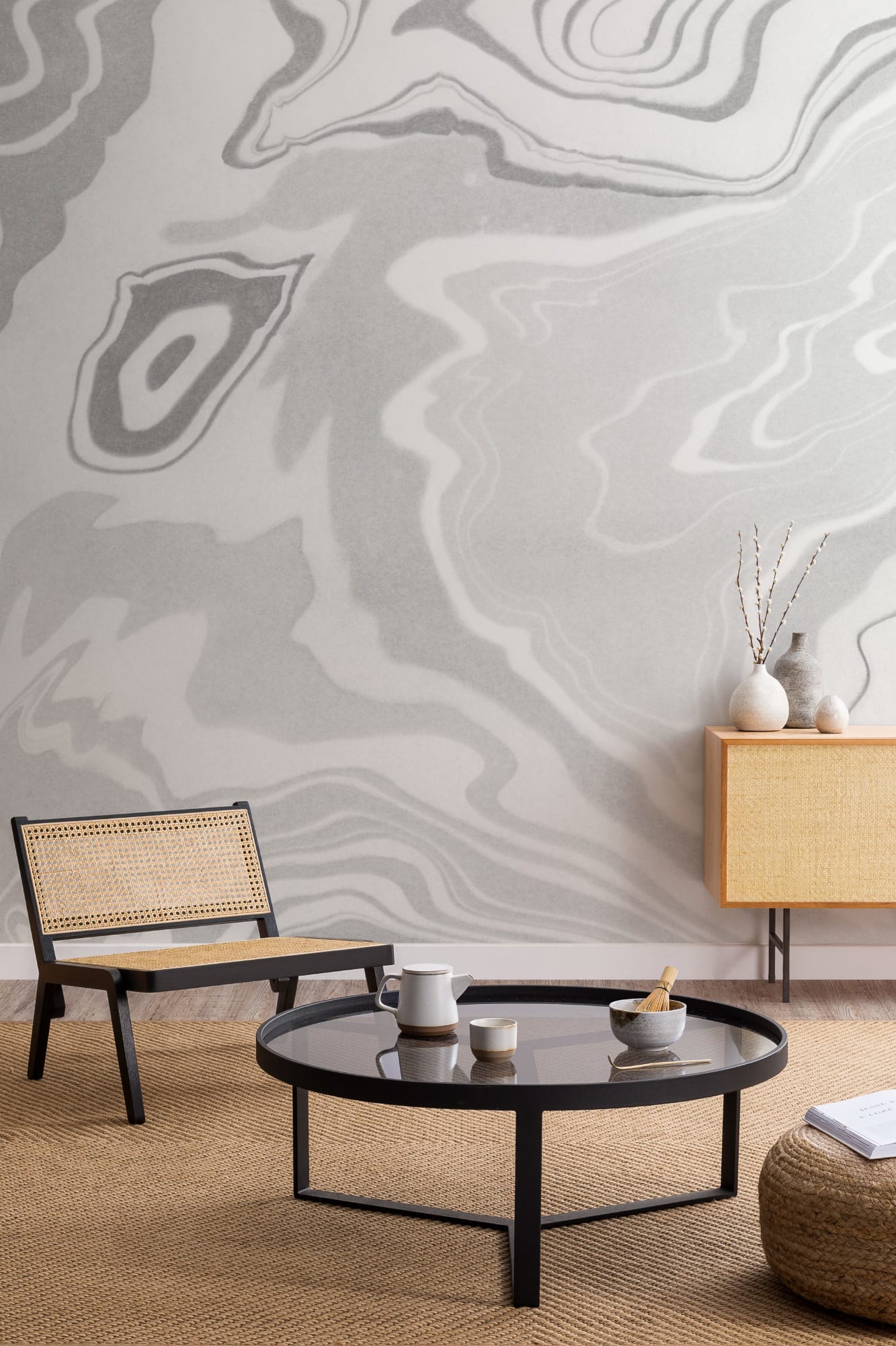 A grey marbled wallpaper in a modern living room with a black cane chair, glass coffee table, and rattan sideboard.