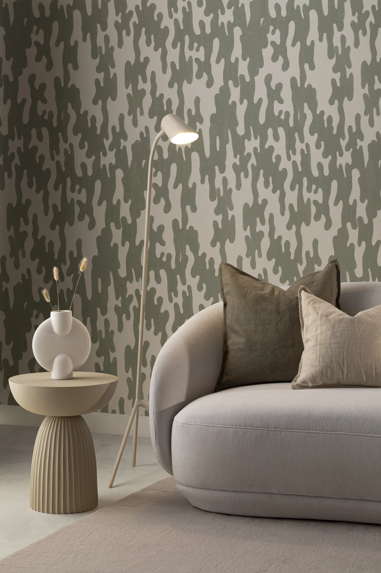 A green and beige abstract pattern wallpaper in a cozy living room with a curved sofa and modern floor lamp.