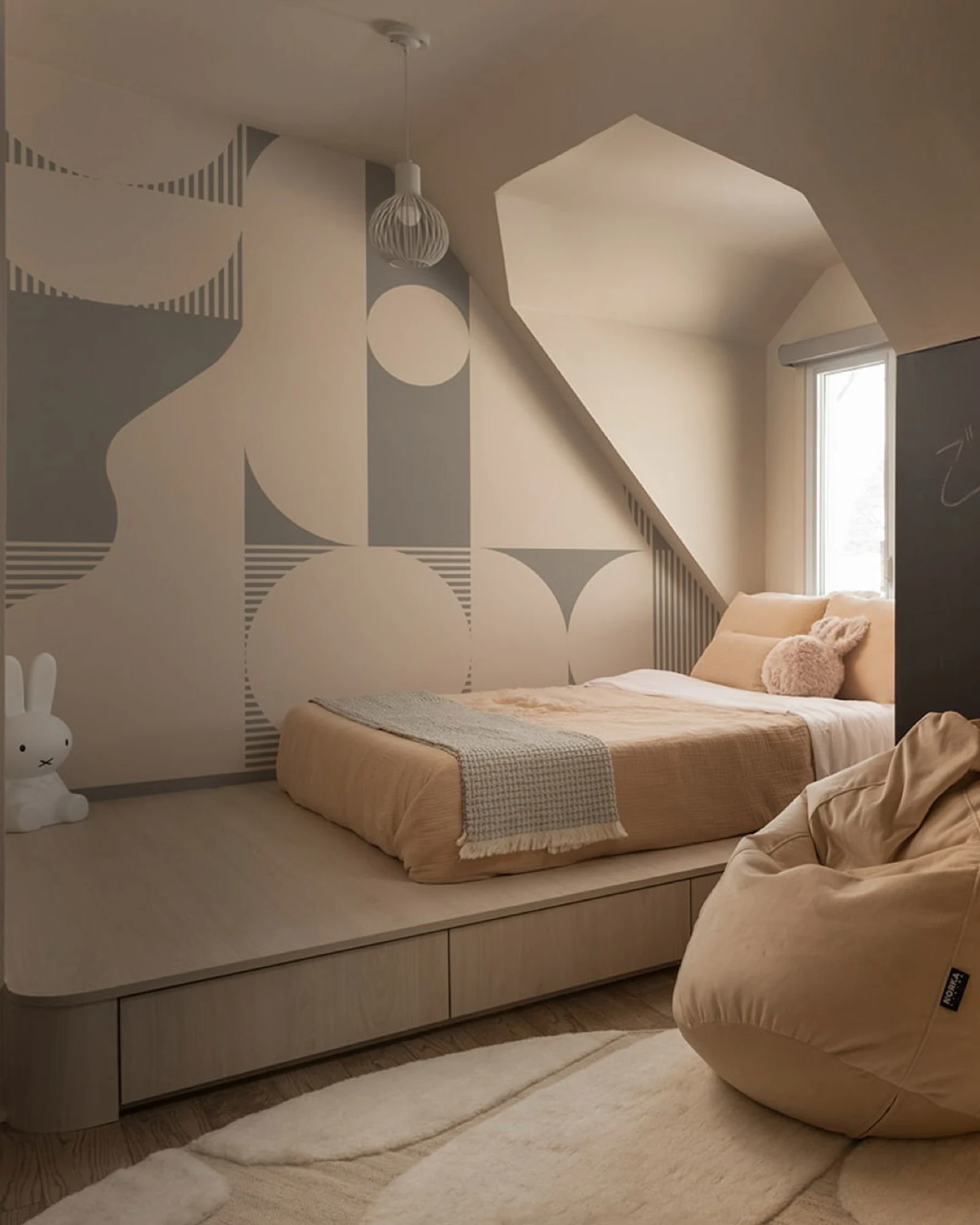 A cozy bedroom nook featuring a geometric accent wall, a white dresser, and a collection of plush toys.