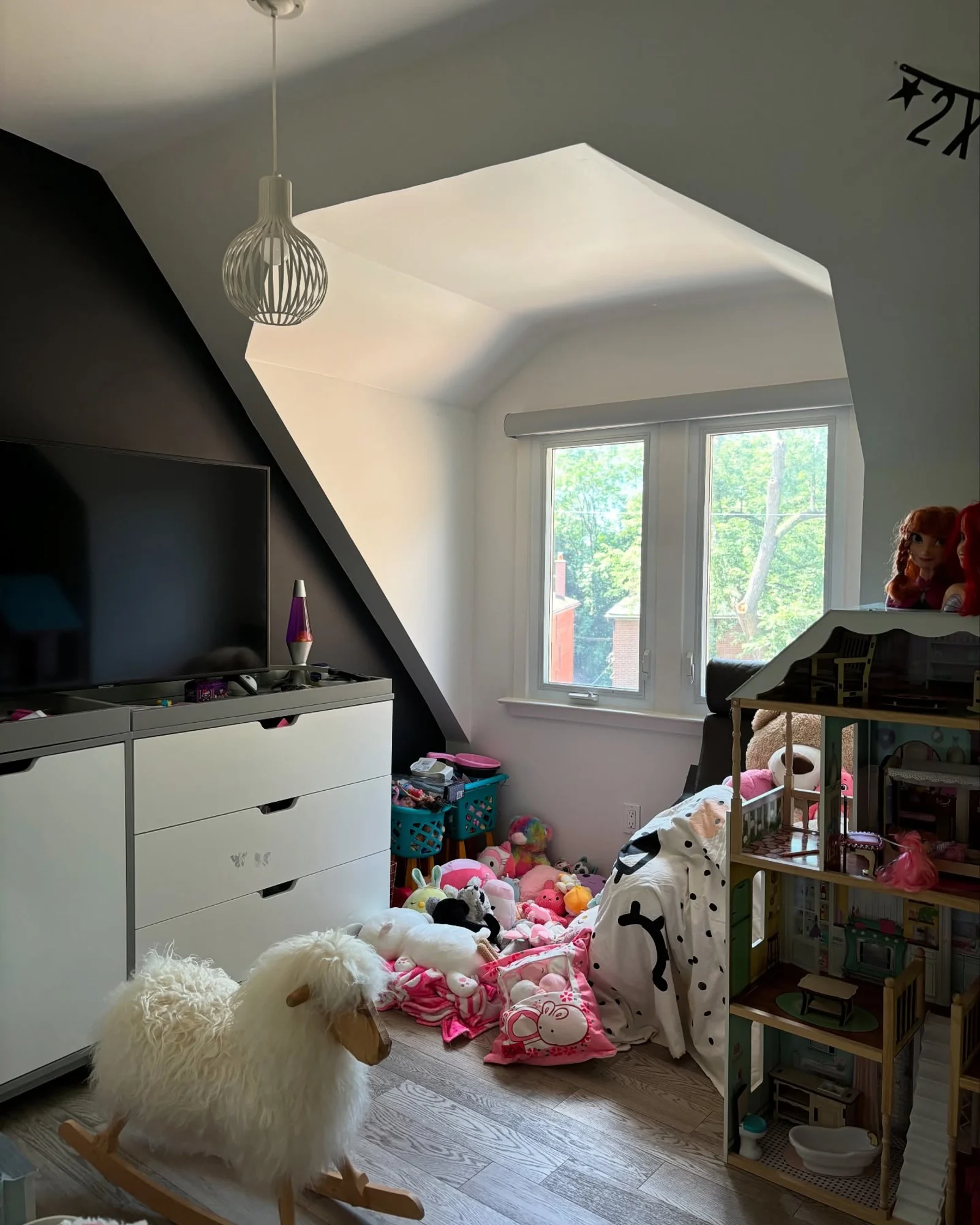 A bedroom corner with a sloped ceiling, a black accent wall, and a white dresser with stuffed animals on the floor.