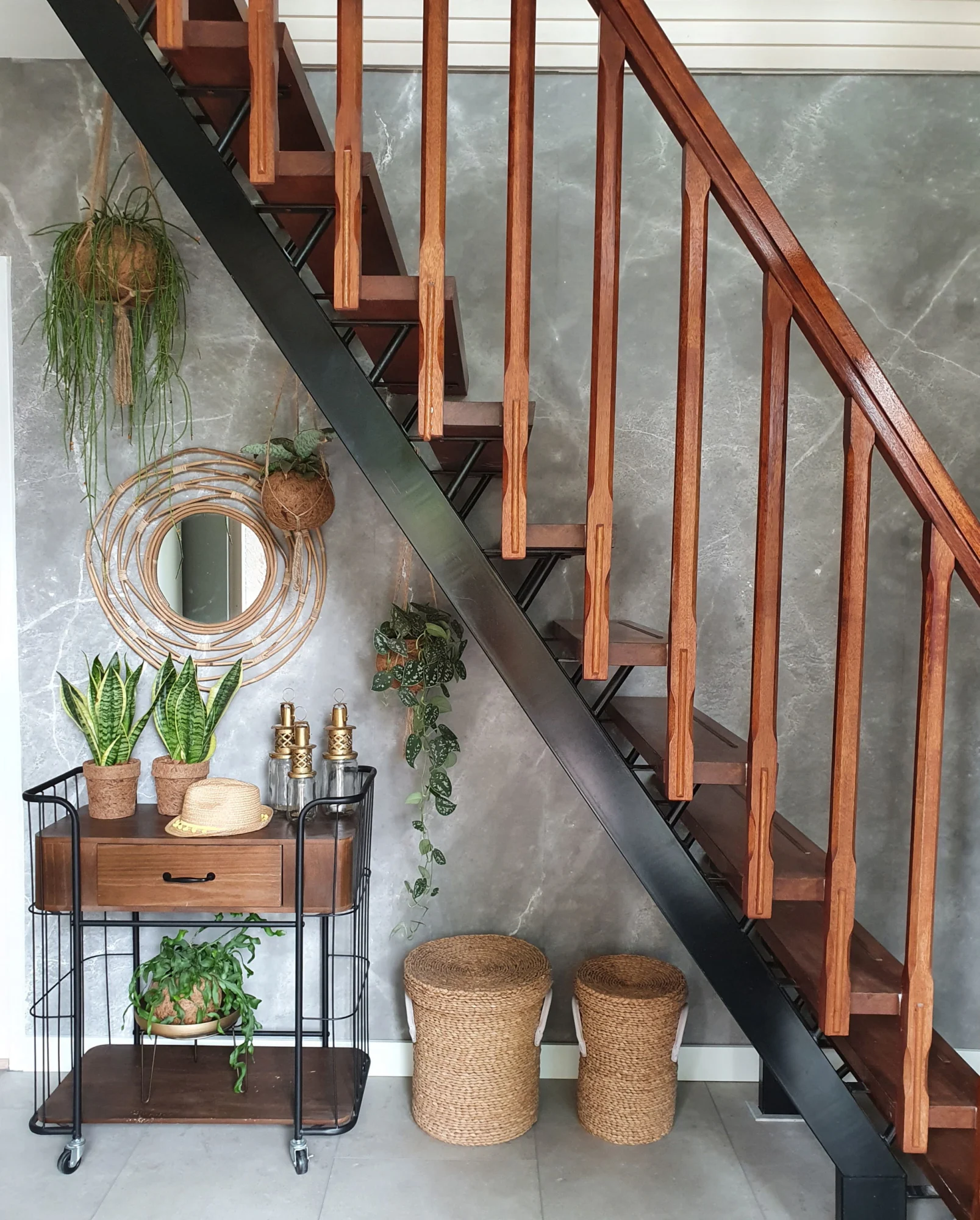 A staircase landing with a grey marbled wallpaper, wooden stairs, and decorative plants in woven baskets.