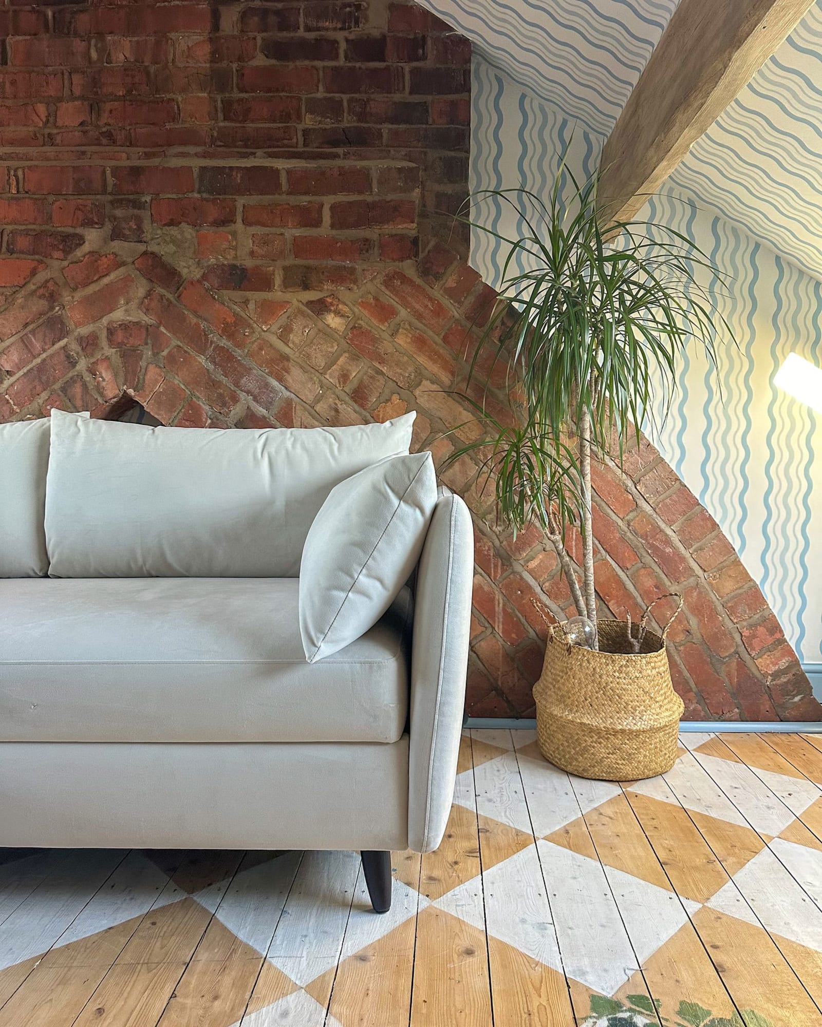 A loft-style living space with a curved brick accent wall, blue and white striped wallpaper, and a light gray sofa.