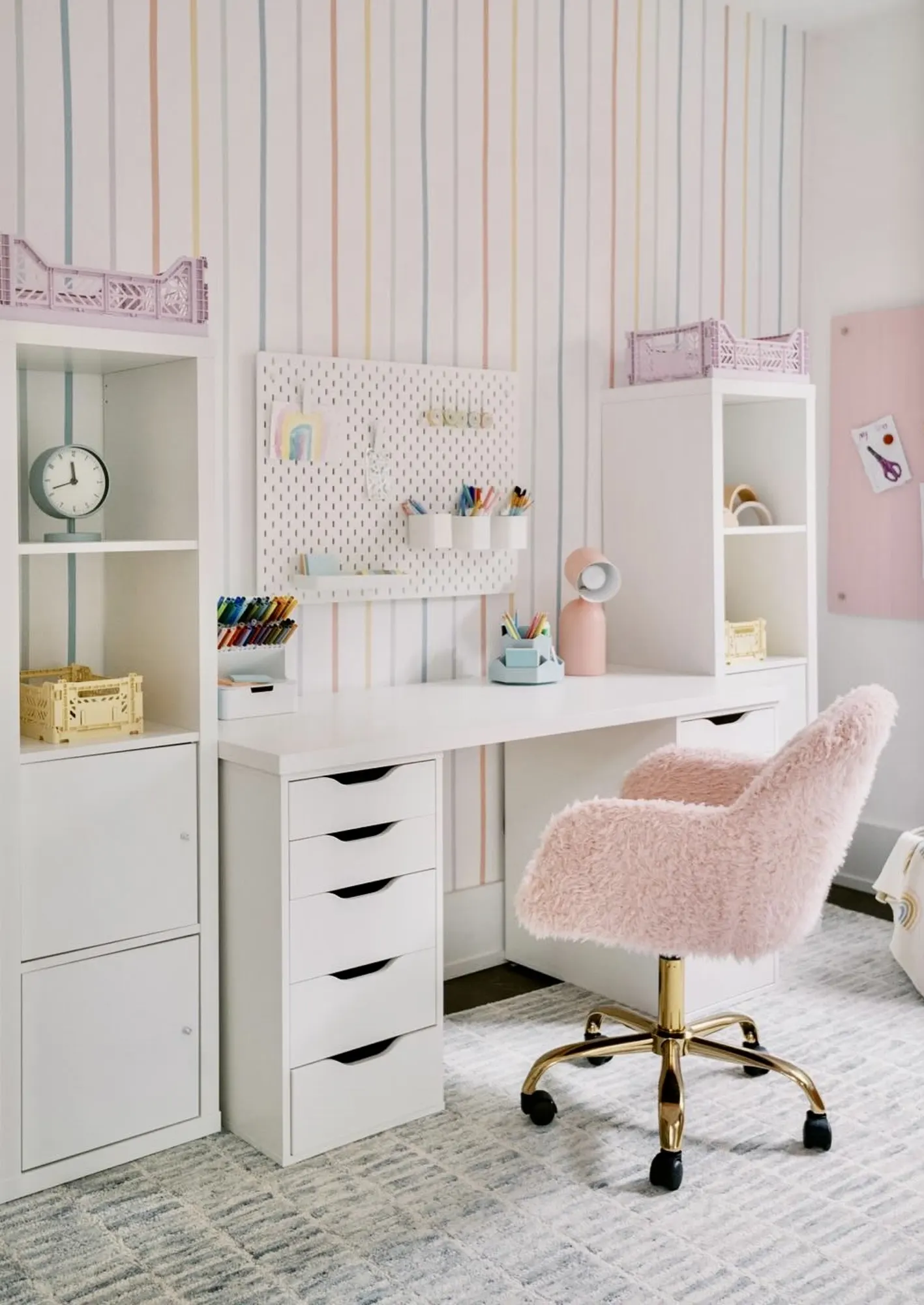A stylish teen study space with vertical pastel-striped wallpaper, a white desk, and a pink faux fur chair.