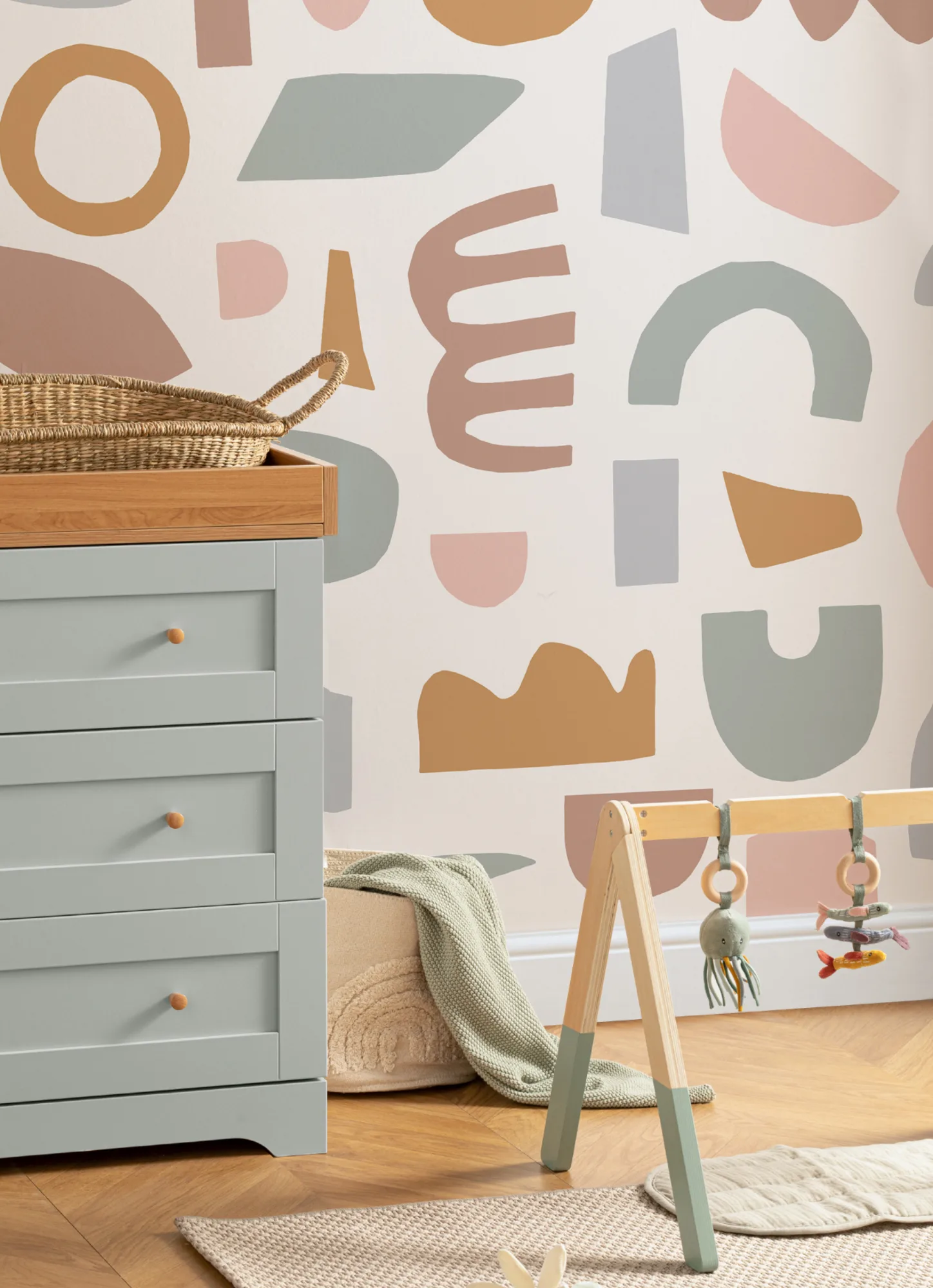 A cozy nursery with a soft-toned abstract wallpaper, a sage green changing table, and a wooden baby gym.