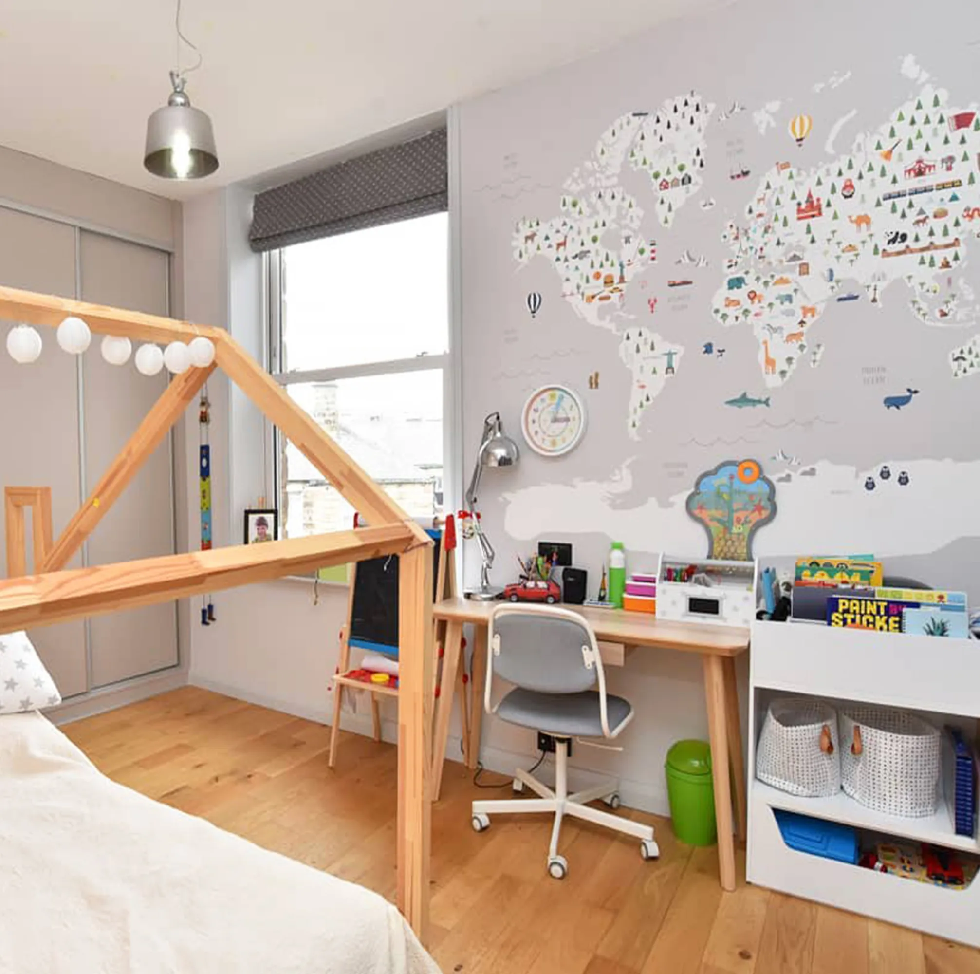 A modern teen bedroom with a colorful world map mural, a wooden house-frame bed, and a study desk.