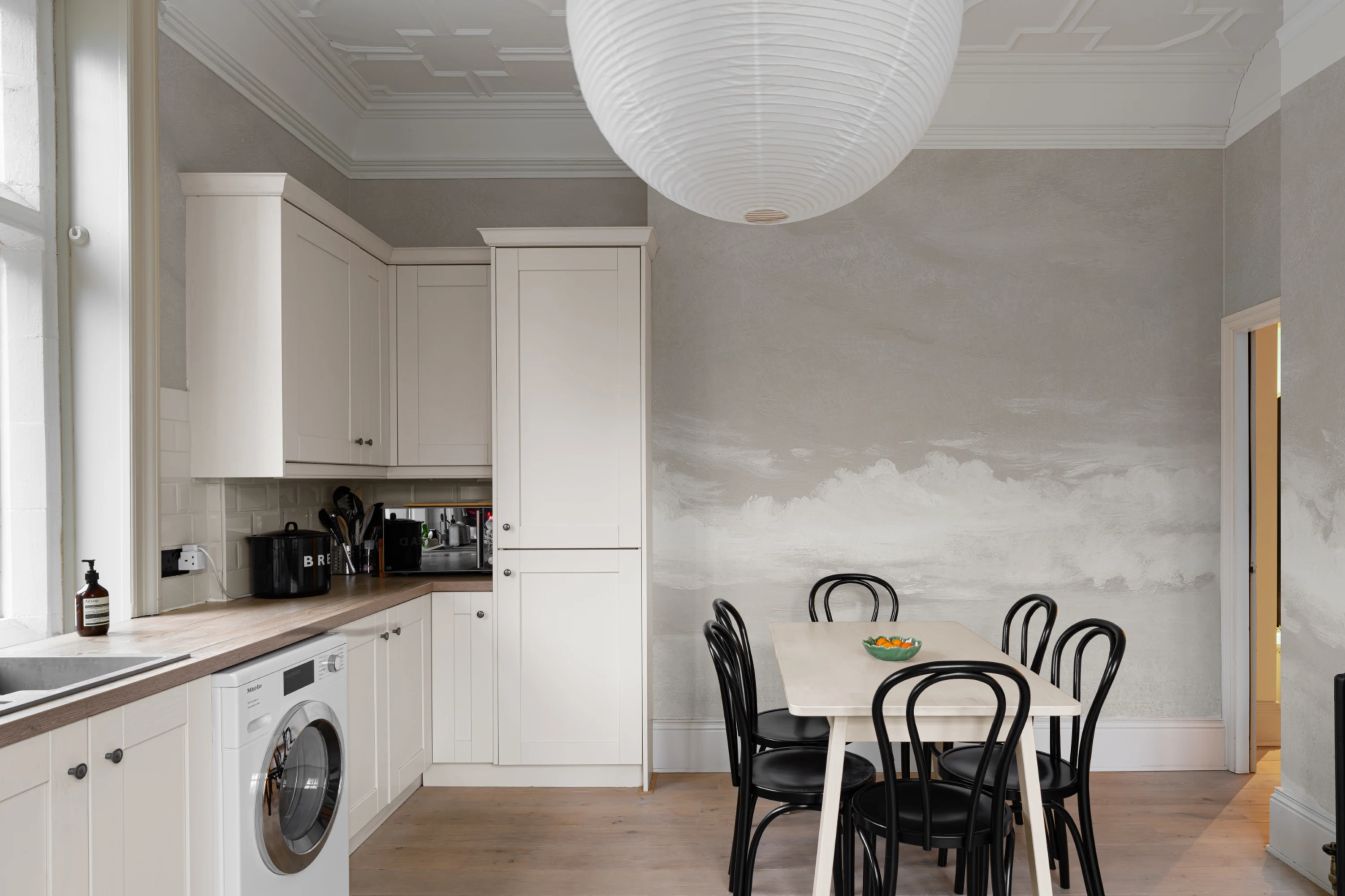 Neutral-toned kitchen with cloud-like mural and black dining chairs around a light wooden table.
