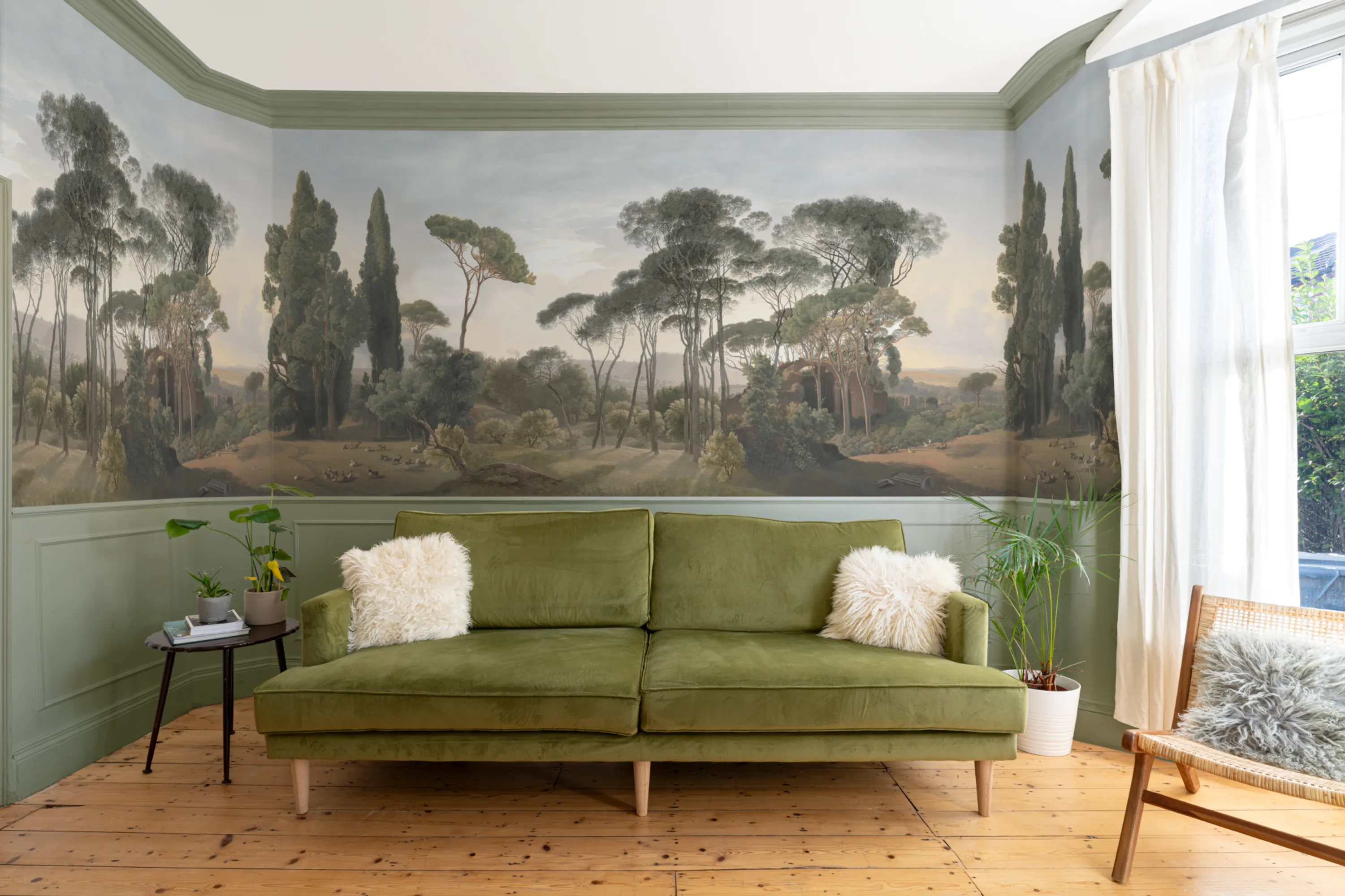 Living room featuring a panoramic mural of a classical forest scene with an olive green sofa.