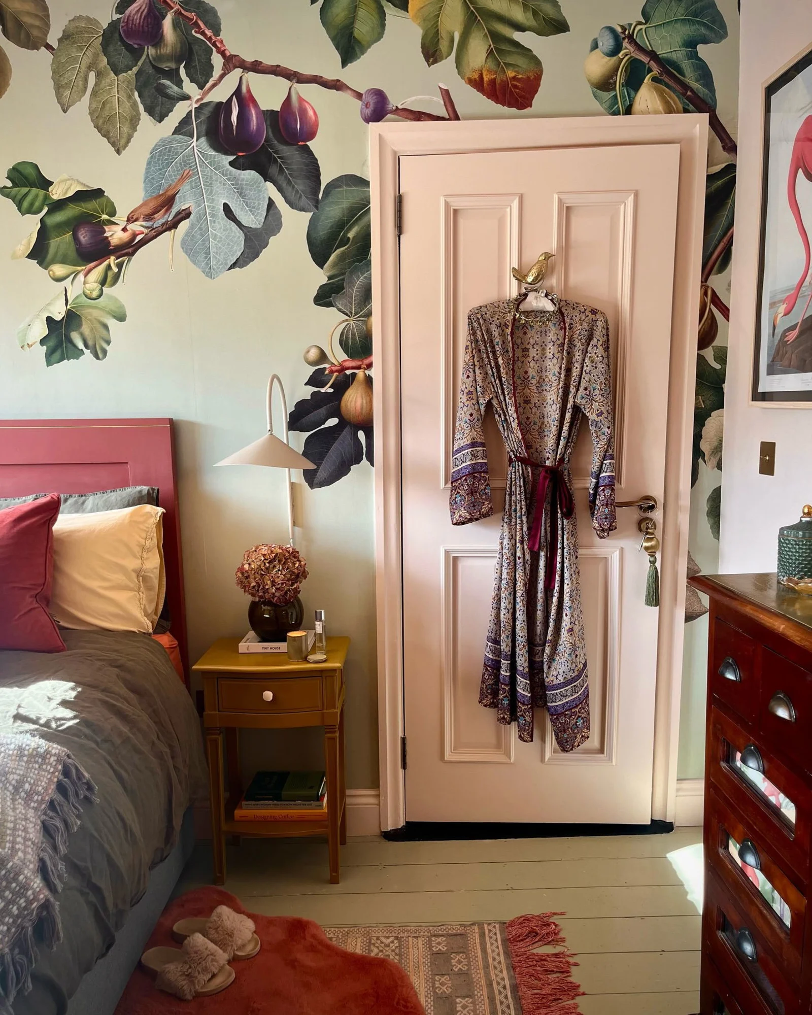 A warm, inviting bedroom with a pink botanical wallpaper behind a gingham bed and mint green nightstand.
