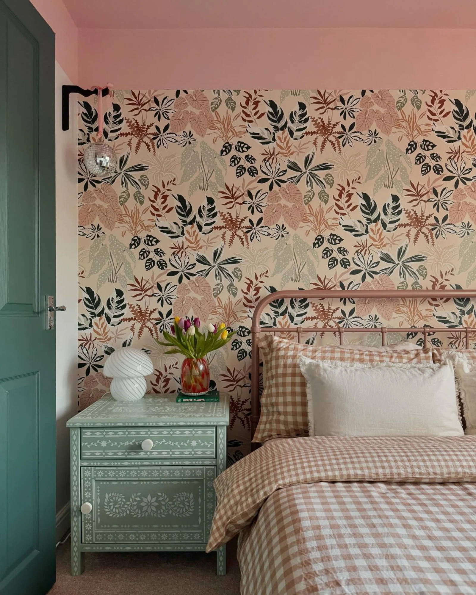 A cozy bedroom corner featuring a sample botanical wallpaper taped above a red headboard.