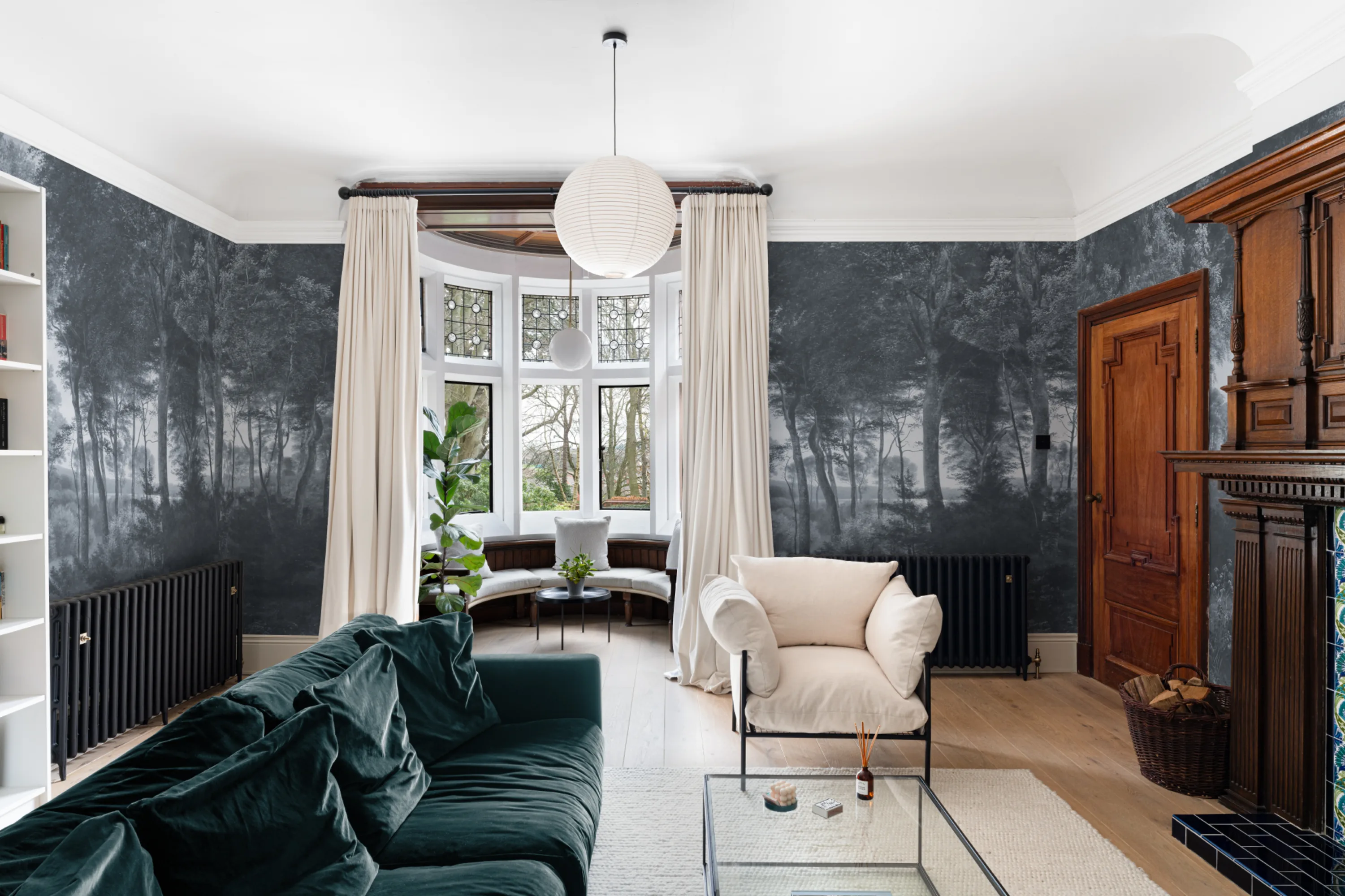 Living room with dark green velvet sofa and white armchair set against a dramatic grayscale forest mural.