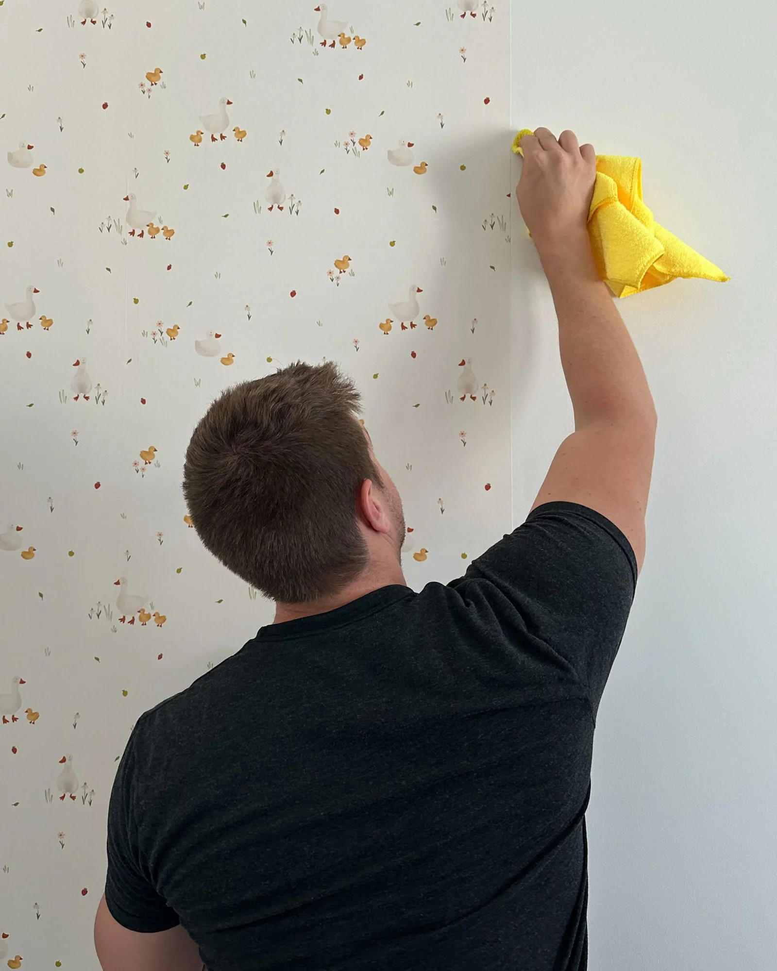 A man installing peel-and-stick wallpaper to a nursery wall.