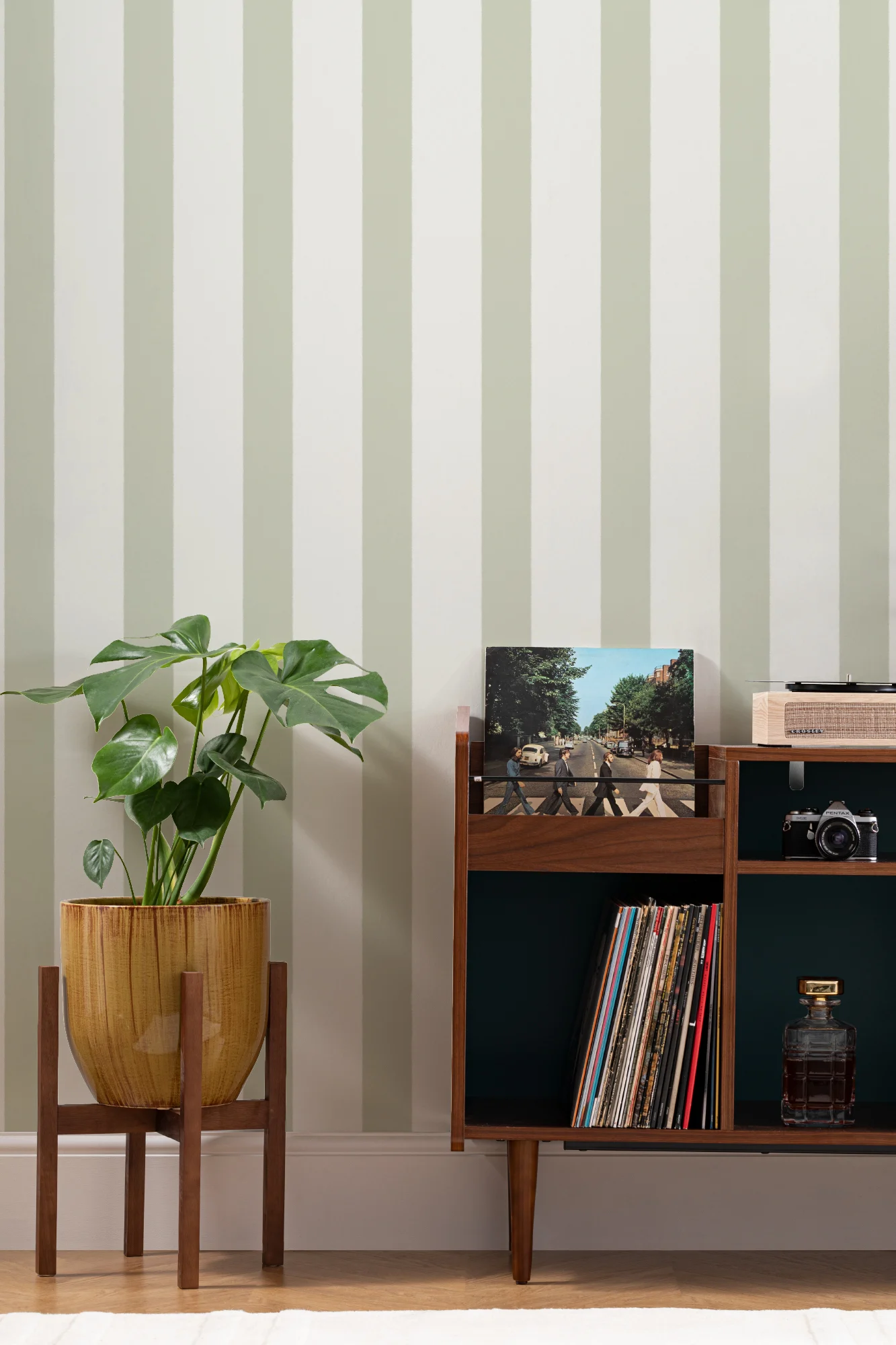 A modern interior with vertical green stripe wallpaper, a potted plant, and a mid-century record cabinet.