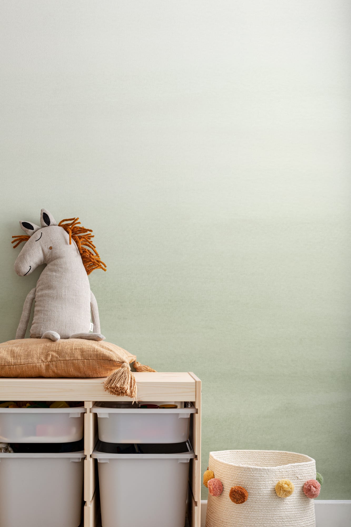 A pale green ombre wallpaper behind storage bins, with a stuffed horse toy resting on a pillow.