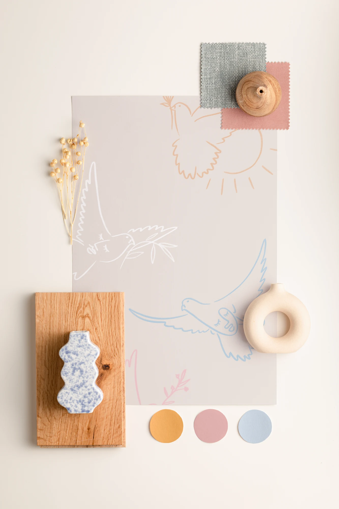 A calming, soft color moodboard featuring a dove-print wallpaper sample, pastel fabric swatches, dried flowers, wooden accents, and paint chips.