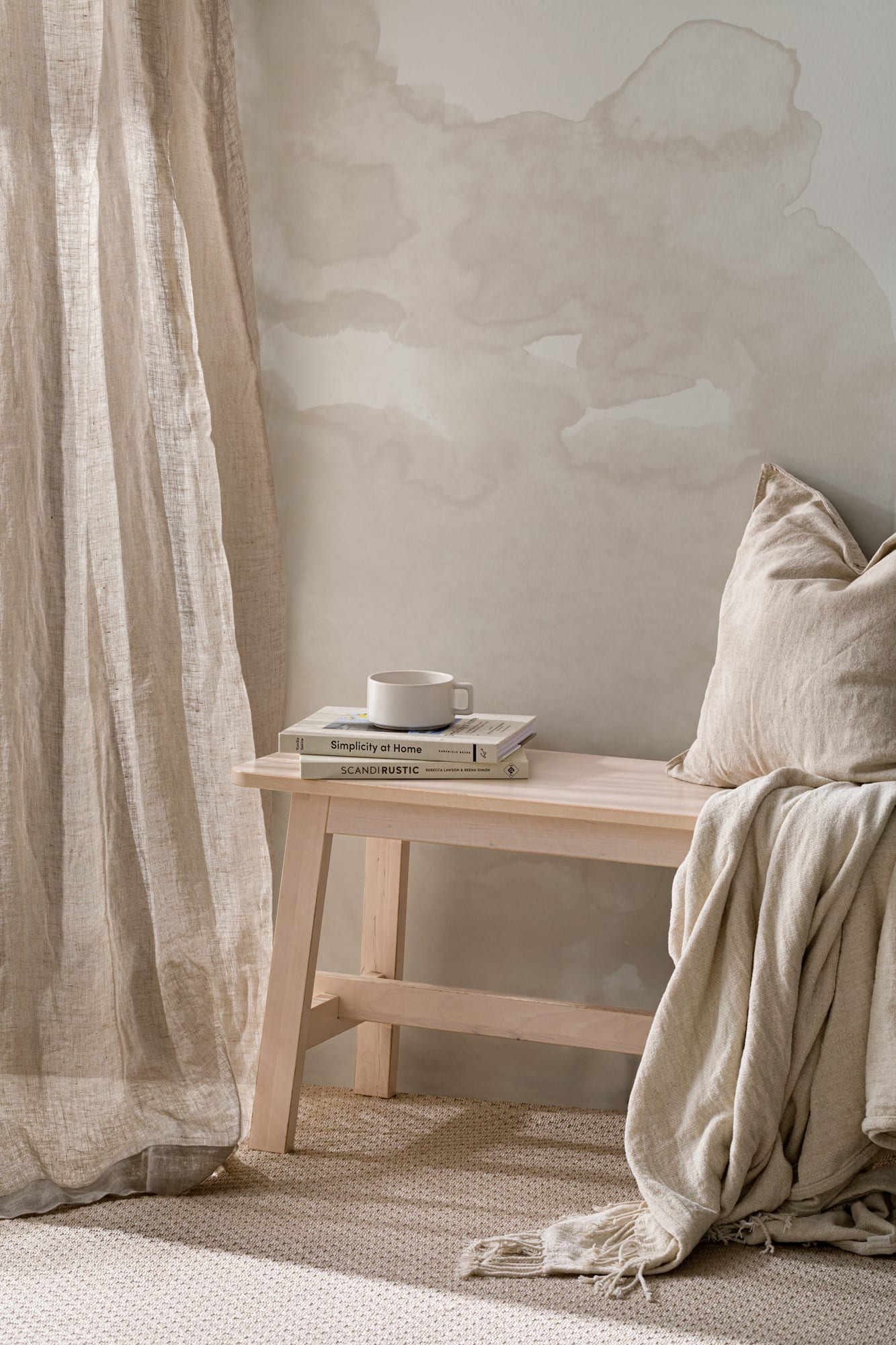 A neutral-toned watercolor mural with a wooden bench, linen cushion, curtain, and books styled in a calming corner.