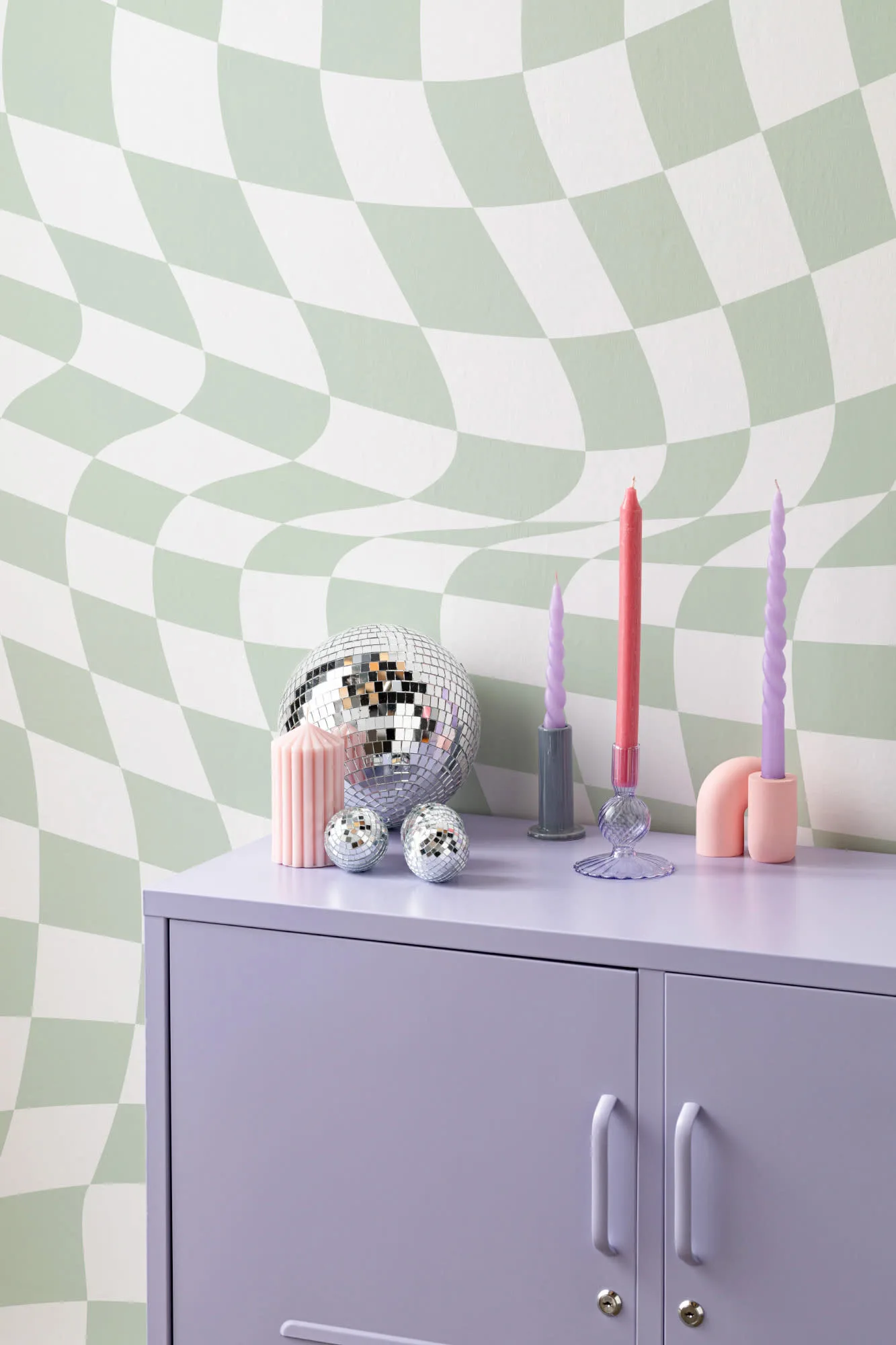 A wavy green and white check wallpaper behind a lavender cabinet with disco balls and colorful candles.