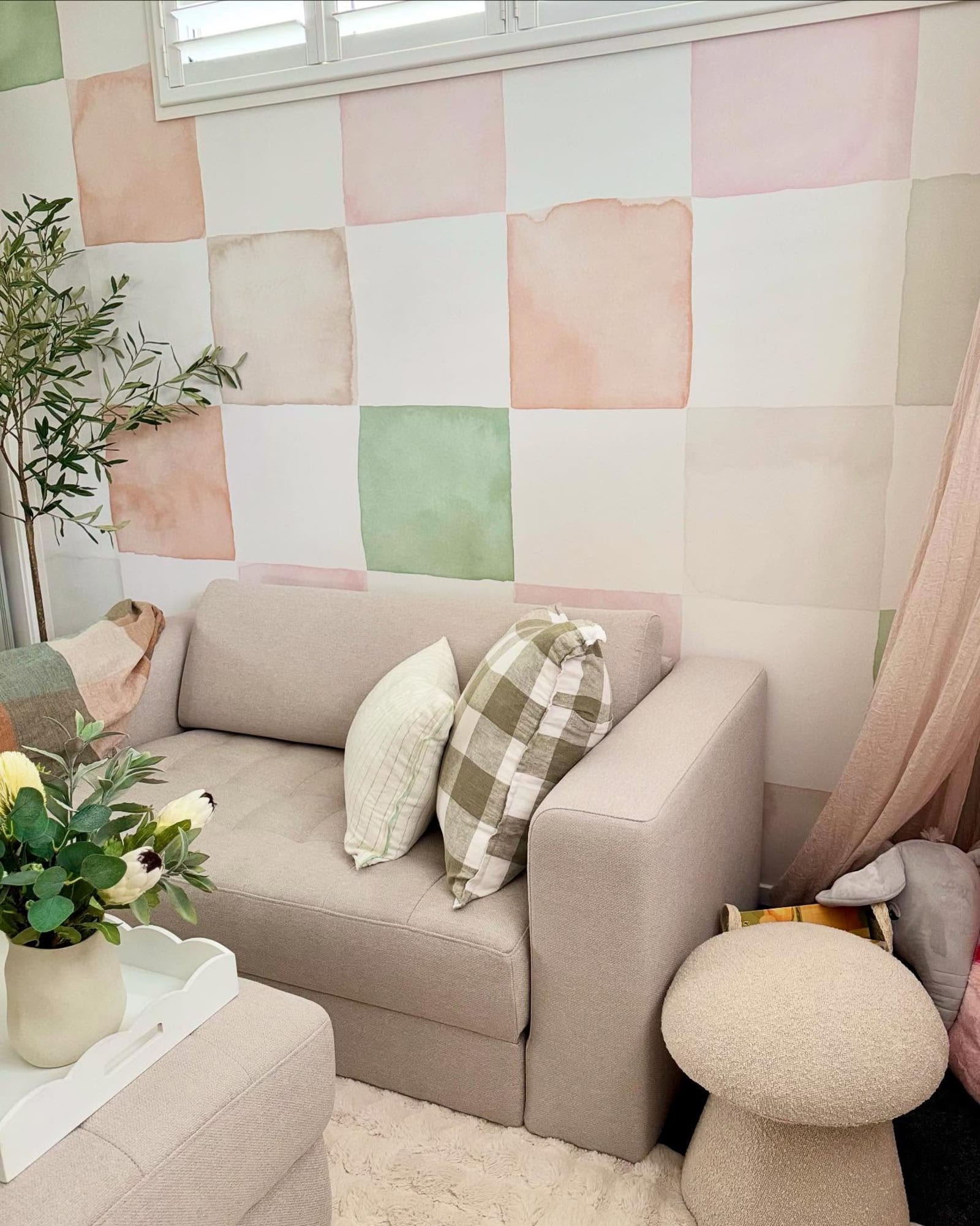A soft pastel check wallpaper in pink, green, and peach hues decorates a cozy living room corner.