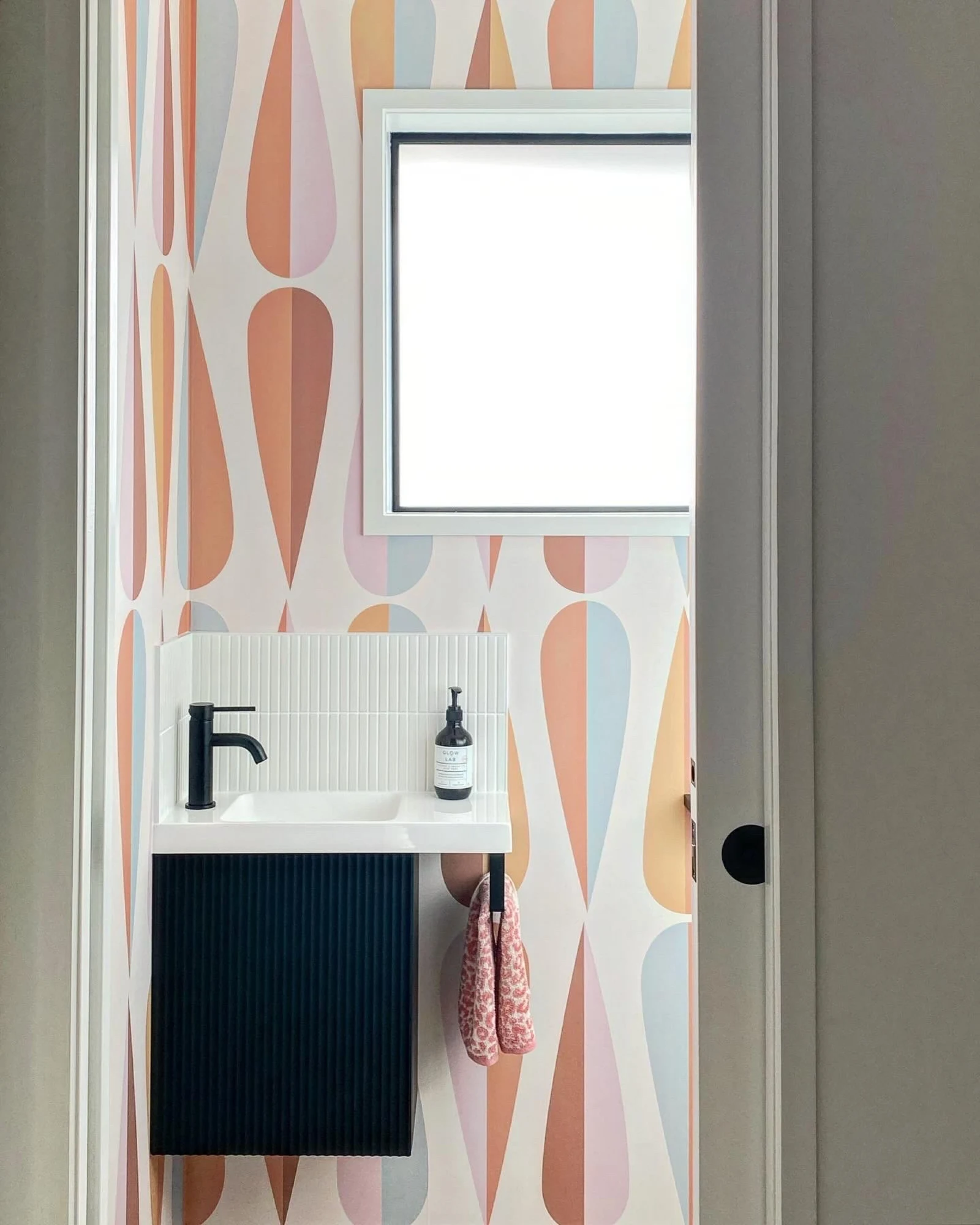 Small bathroom with colorful retro droplet-pattern wallpaper and a modern black vanity.