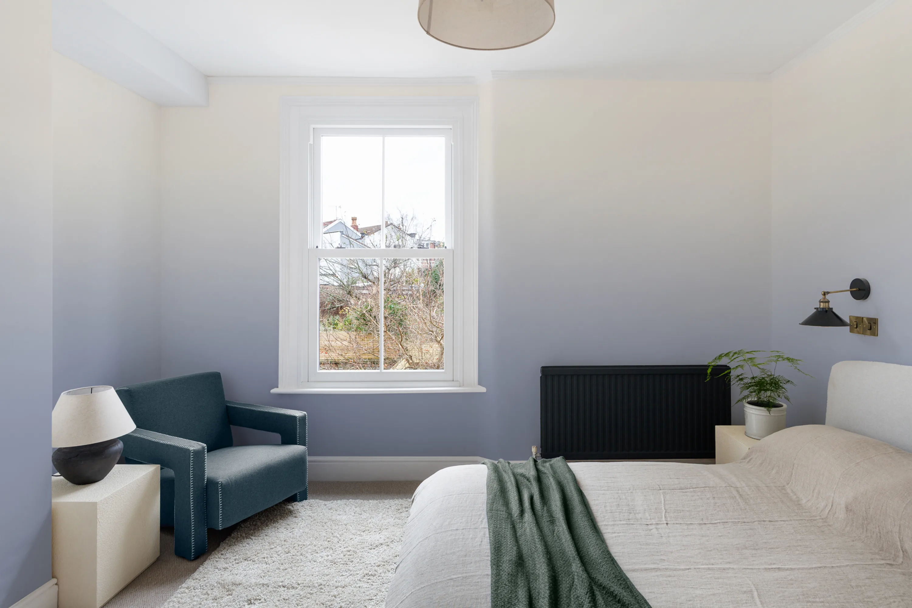 Minimalist bedroom with calming blue ombre wallpaper, a white-framed window, and simple furniture.