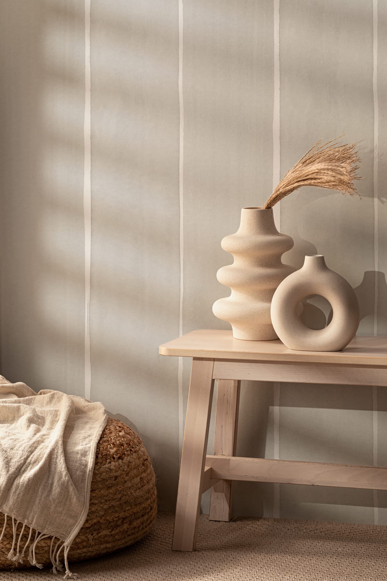 Neutral room with soft striped wallpaper, wooden bench, and sculptural vases in natural tones.