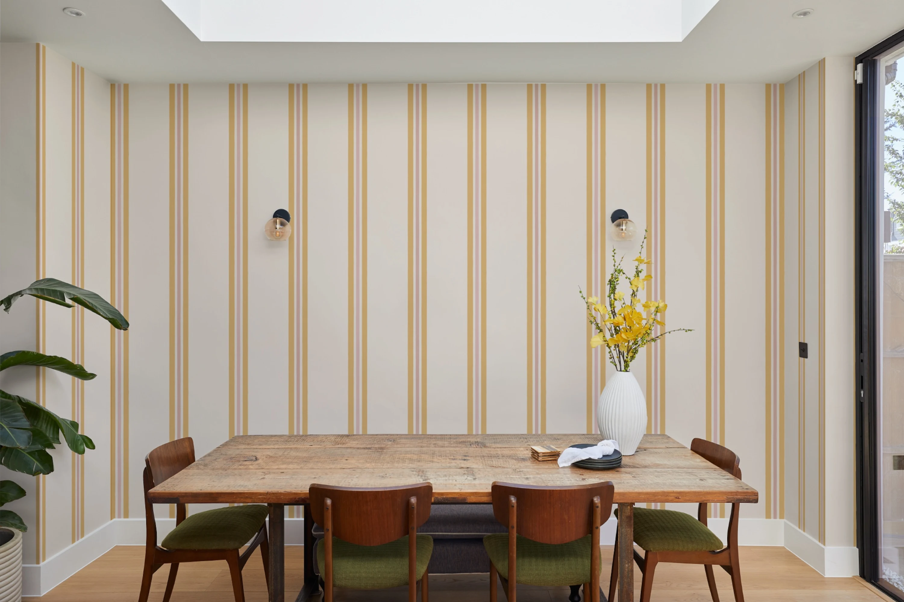 Dining room with vertical mustard-yellow striped wallpaper and a rustic wooden table with mid-century chairs.